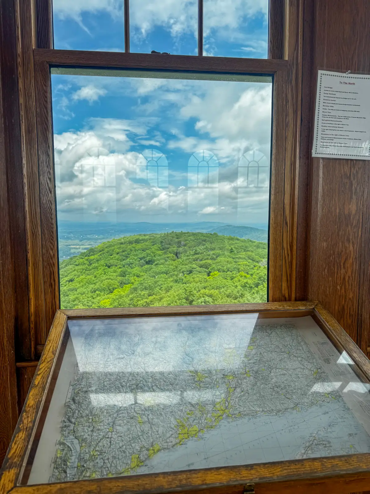 window view from the top floor of heublein tower with rolling bright green hill and blue sky in distance.