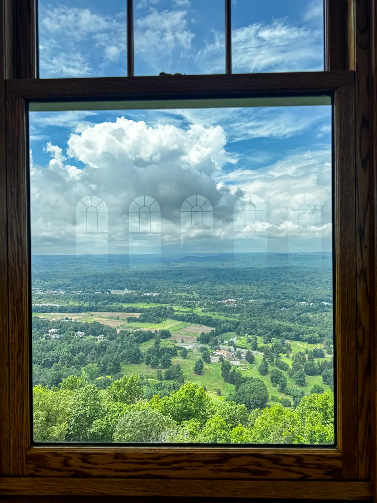 window view from the top floor of heublein tower with rolling bright green hill and blue sky in distance.