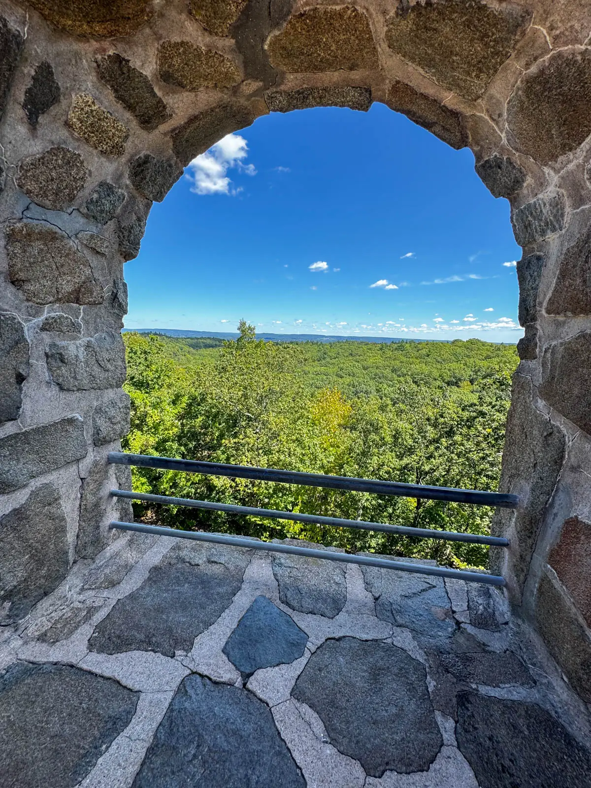 round window opening at top of sleeping giant tower in ct with blue sky and green hills in distance.