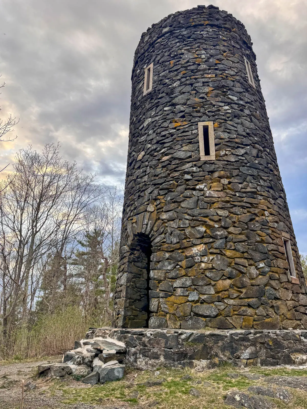 round stone tower with little windows with cloudy sky behind it.