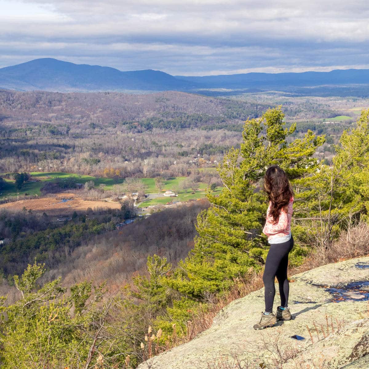 brunette woman on top of cliff edge looking out over mountainous views in late fall in connecticut.