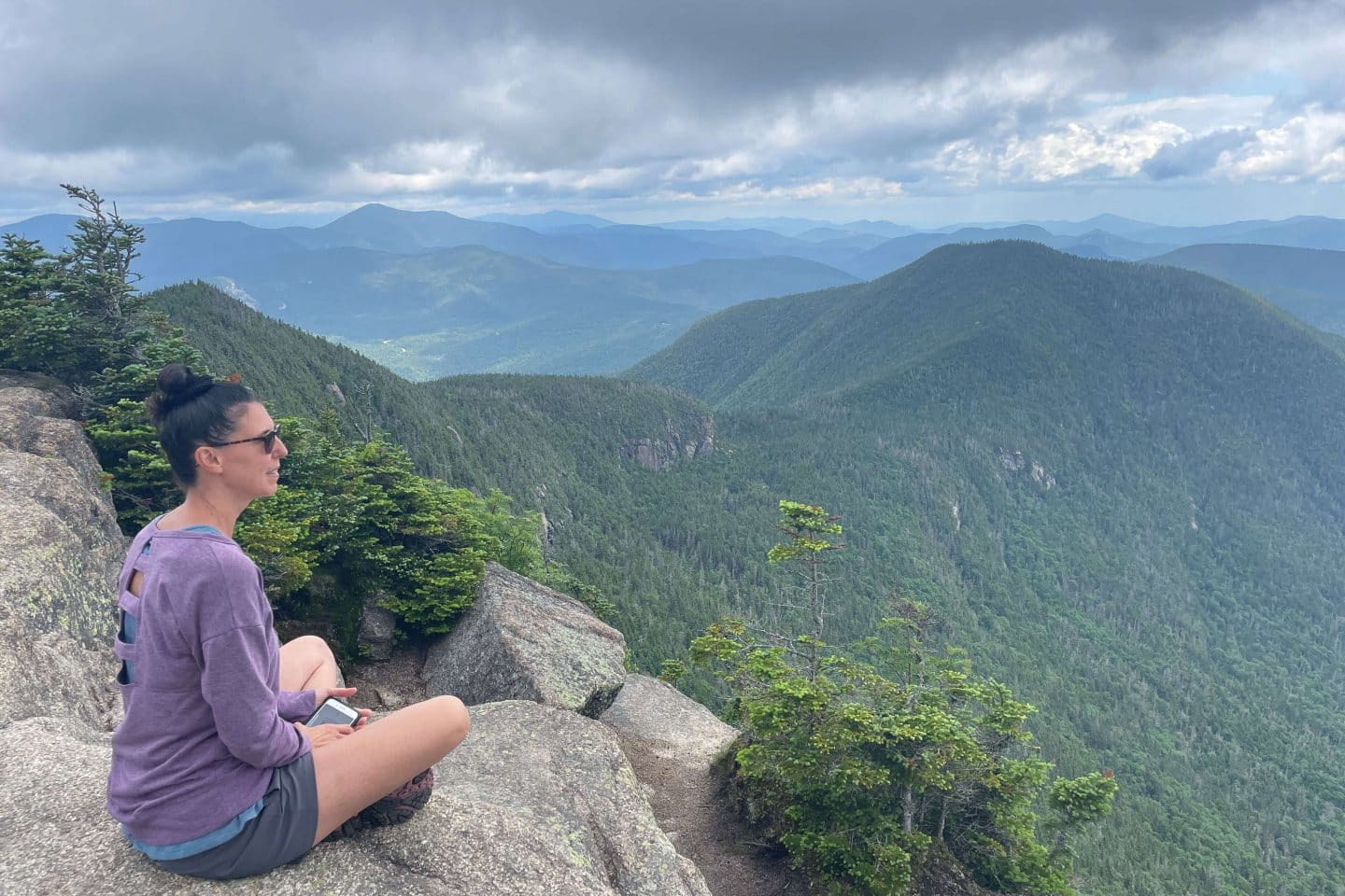 woman sitting on mountain edge amongst green mountains
