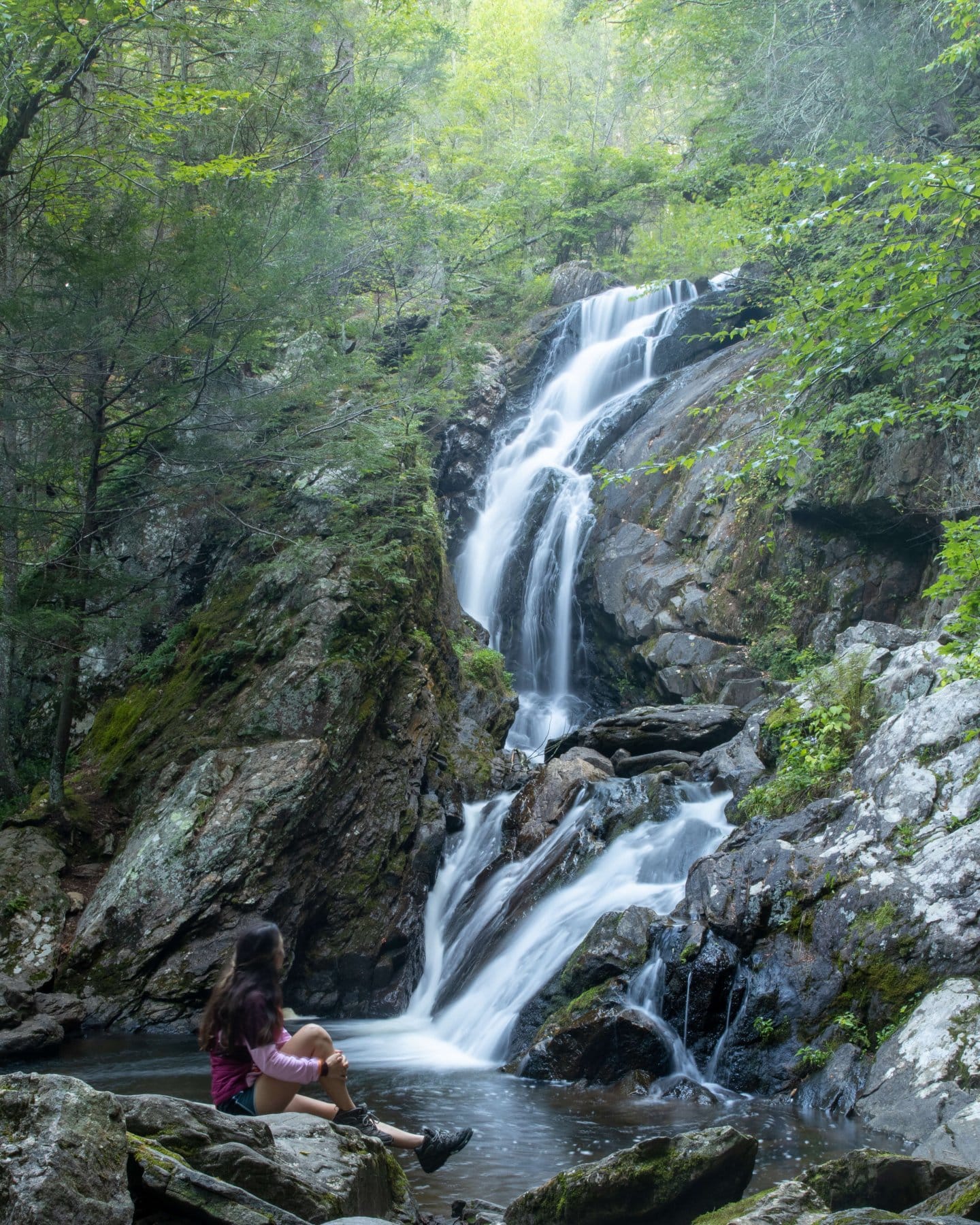 long exposure connecticut waterfall in summer with girl sitting at base of falls