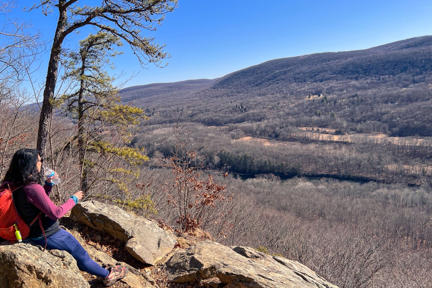 hiking woman on a ledge looking out with blue sky in winter