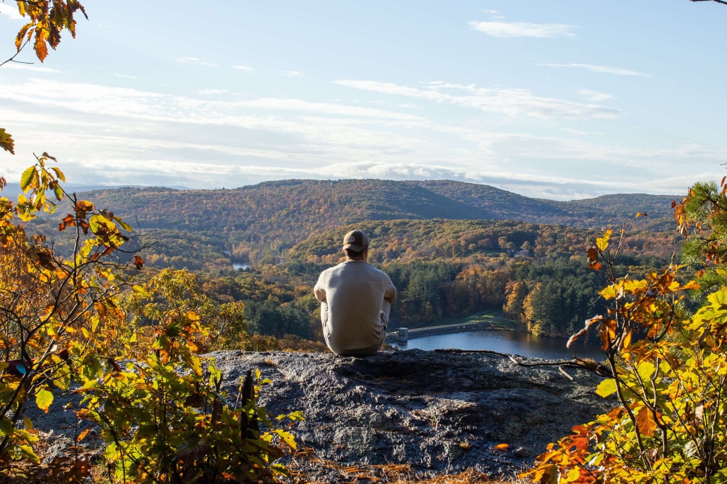 man sitting on hiking ledge with view of blue sky