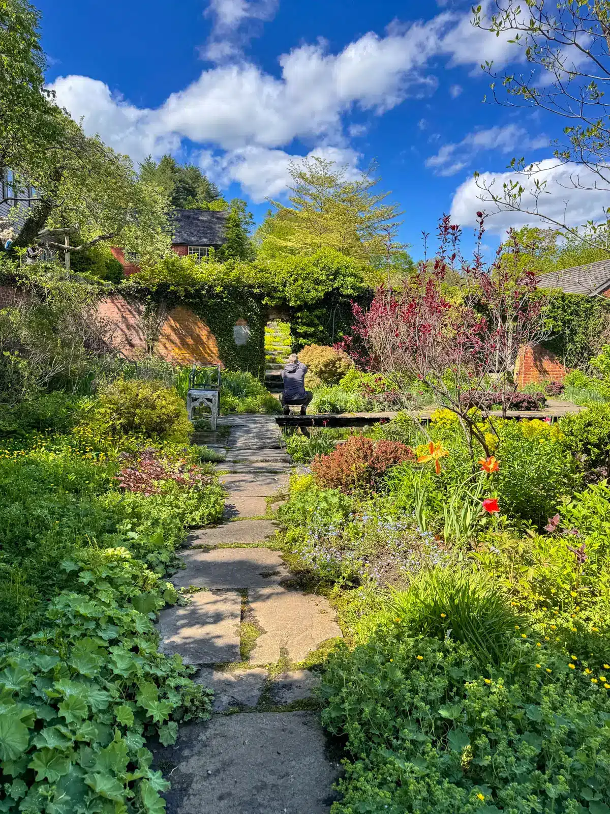 a flower garden at an old mansion in connecticut with stone pathway winding through and bright greenery lining the path with an array of flowers.