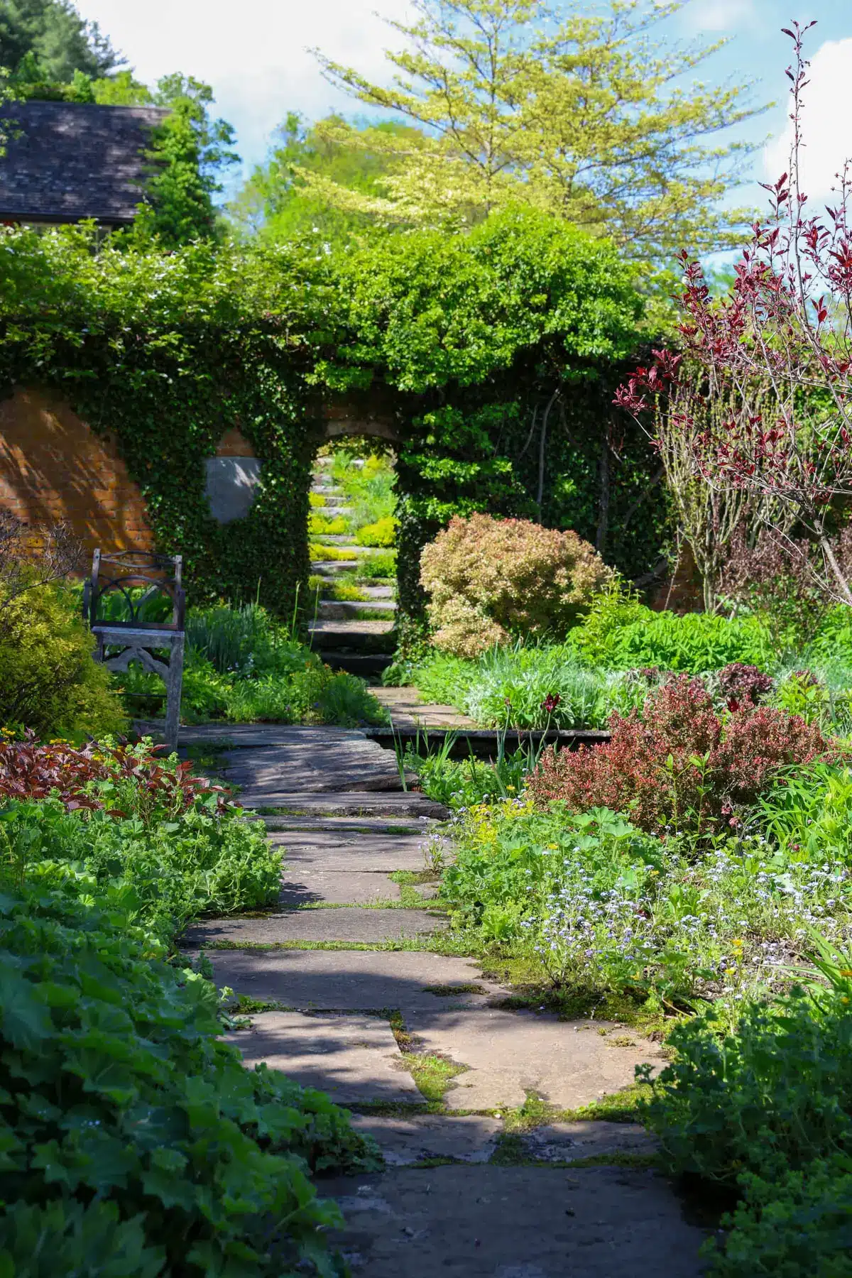 a flower garden at an old mansion in connecticut with stone pathway winding through and bright greenery lining the path with an array of flowers.