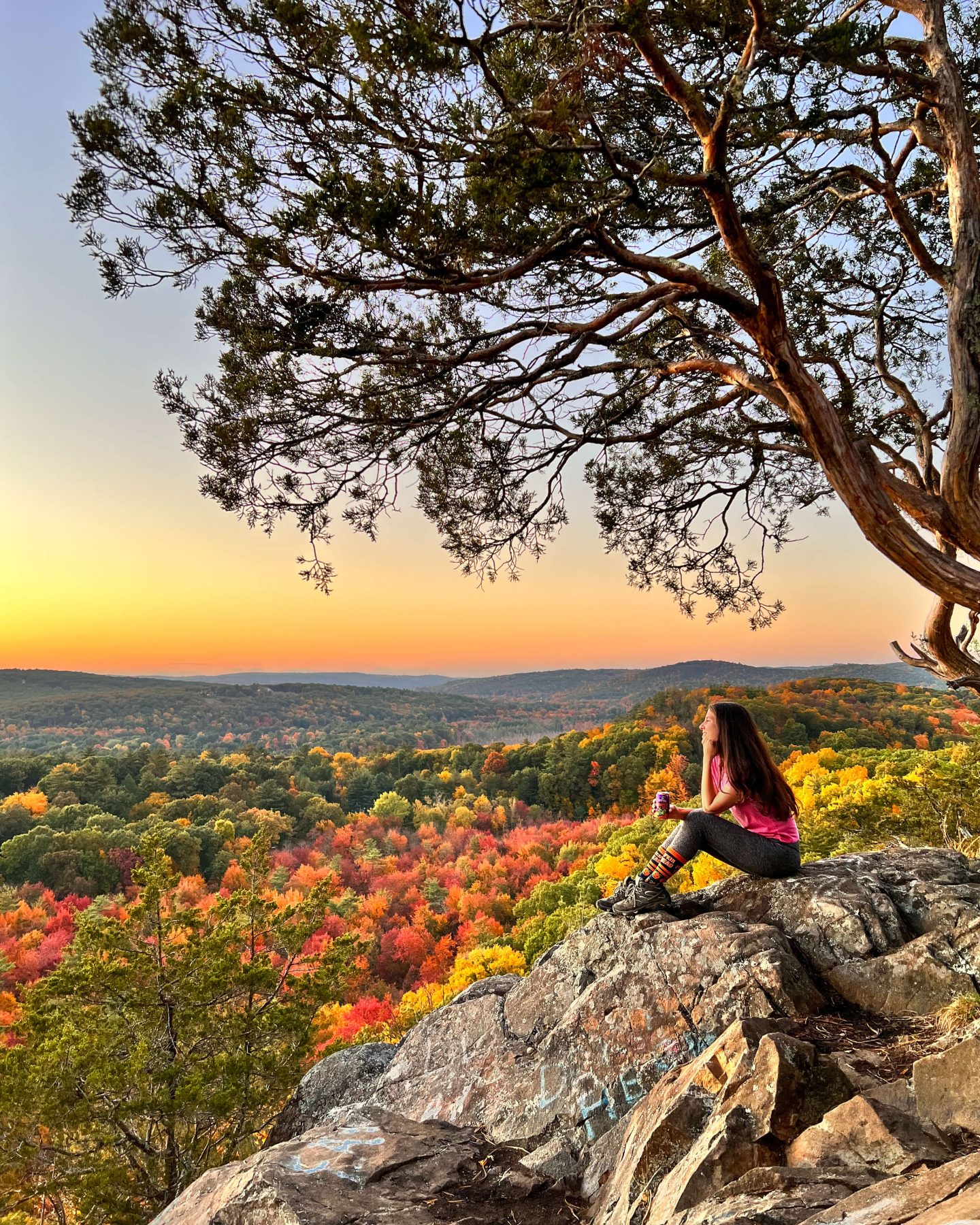 woman sitting on ledge looking out at sunset time in fall surrounded by fall leaves in connecticut