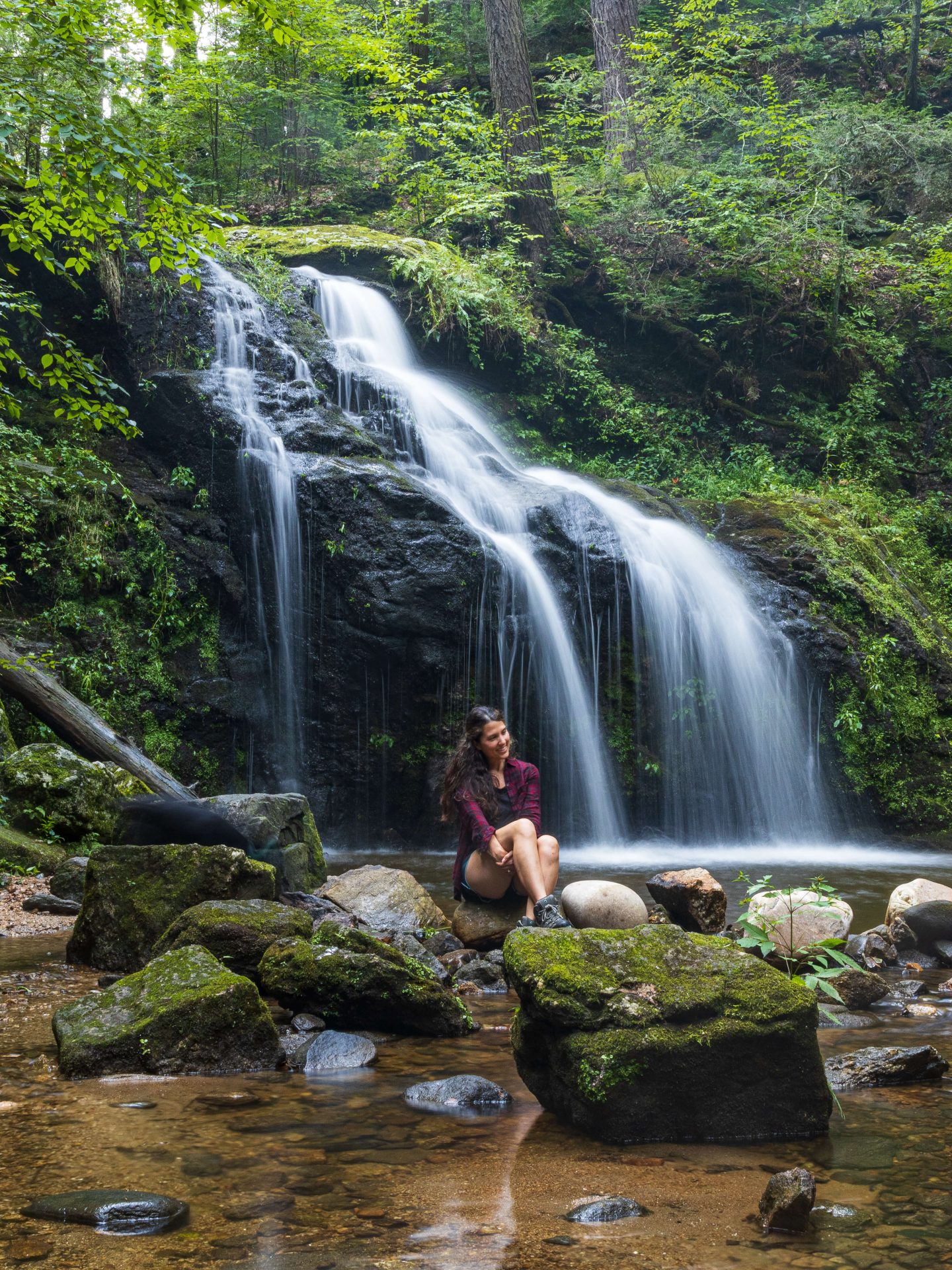 best waterfall in new england with a woman smiling in the summer surrounded by green leaves and trees