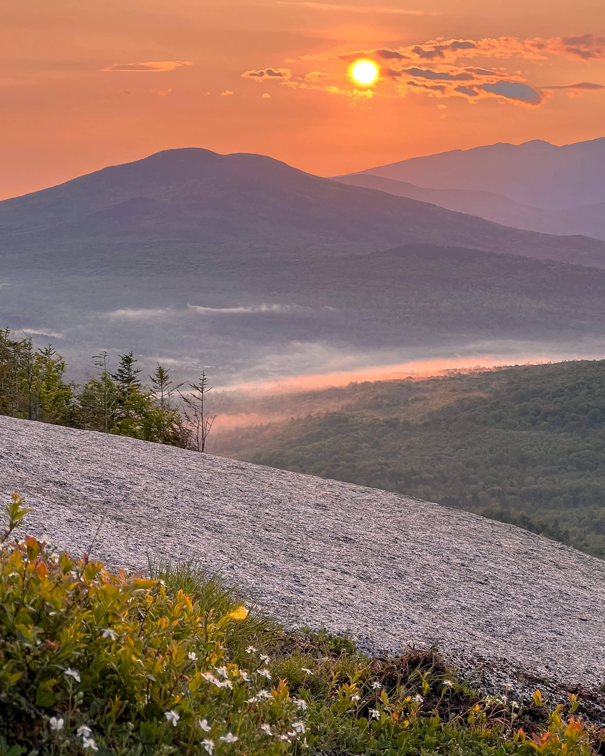 sunrise coming up over layered new hampshire green mountains in summer with some fog below.