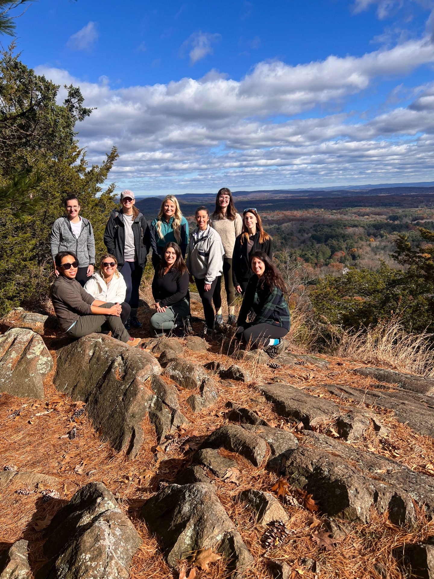 group of female hikers smiling on top of west mountain in simsbury connecticut on a late fall day