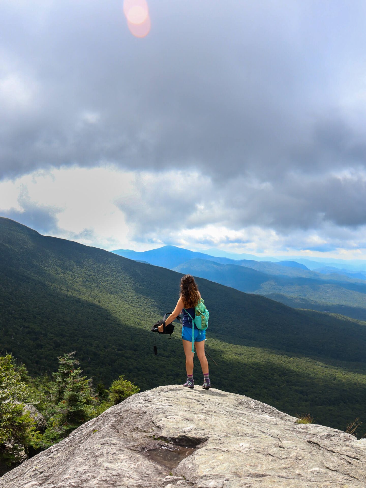 woman at the top of mount mansfield trail in summer surrounded by green trees