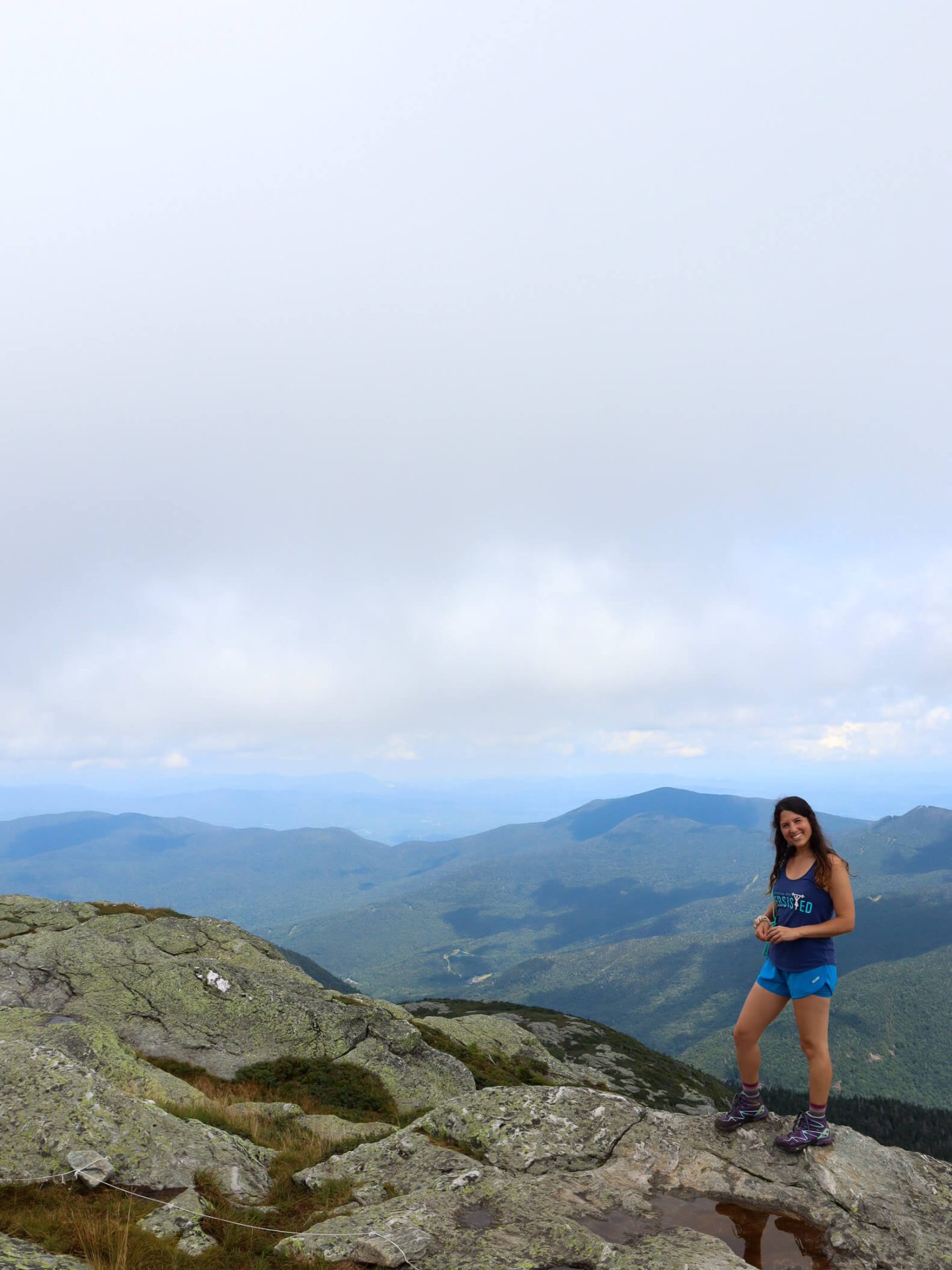 woman standing at the top of mount mansfield in summer with green mountains