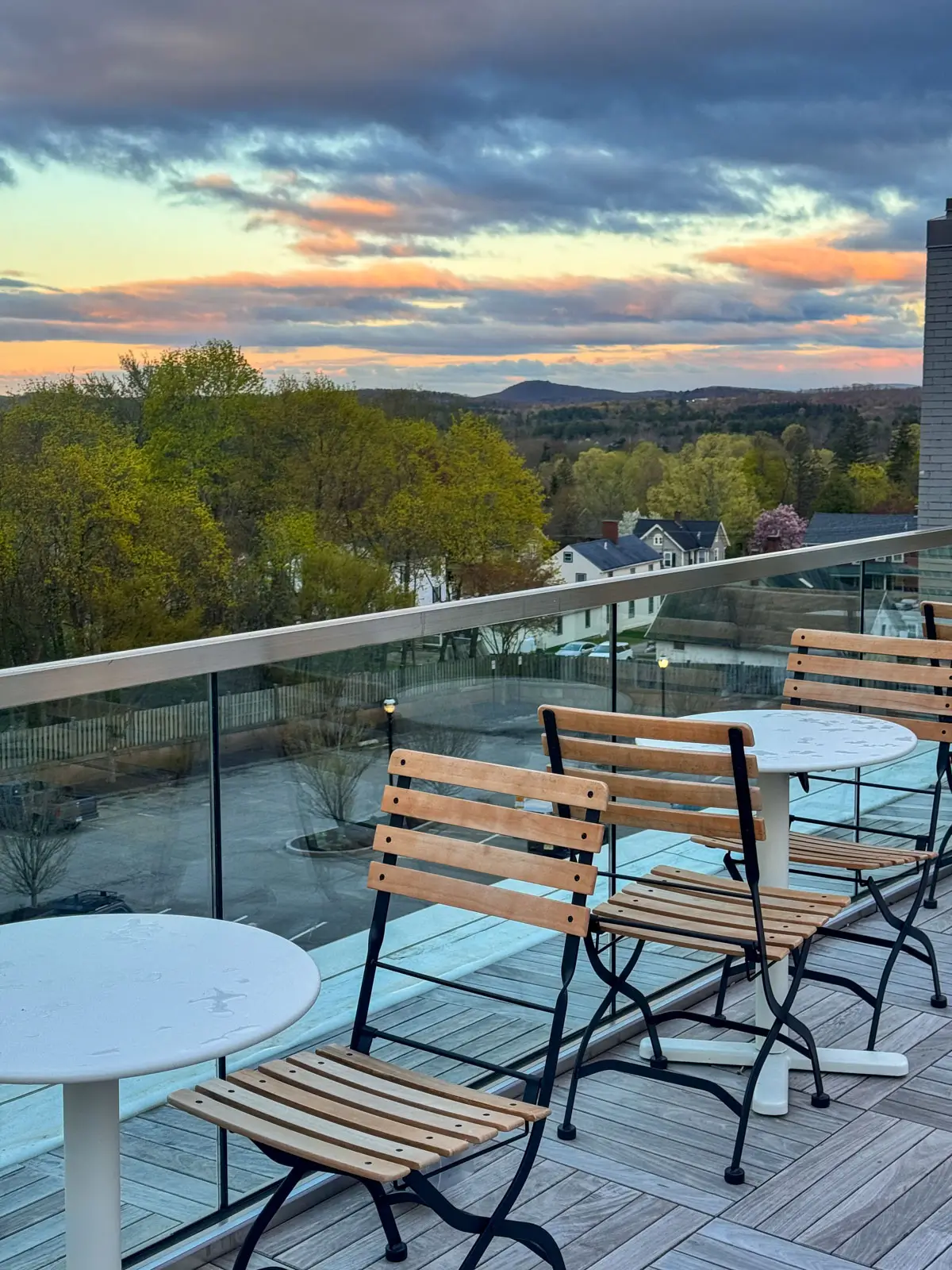rooftop dining at hotel bedroom with king size bed with white comforter and yellow walls at The Abner Hotel in downtown Litchfield, CT with sunset colors in sky and green trees in distance.