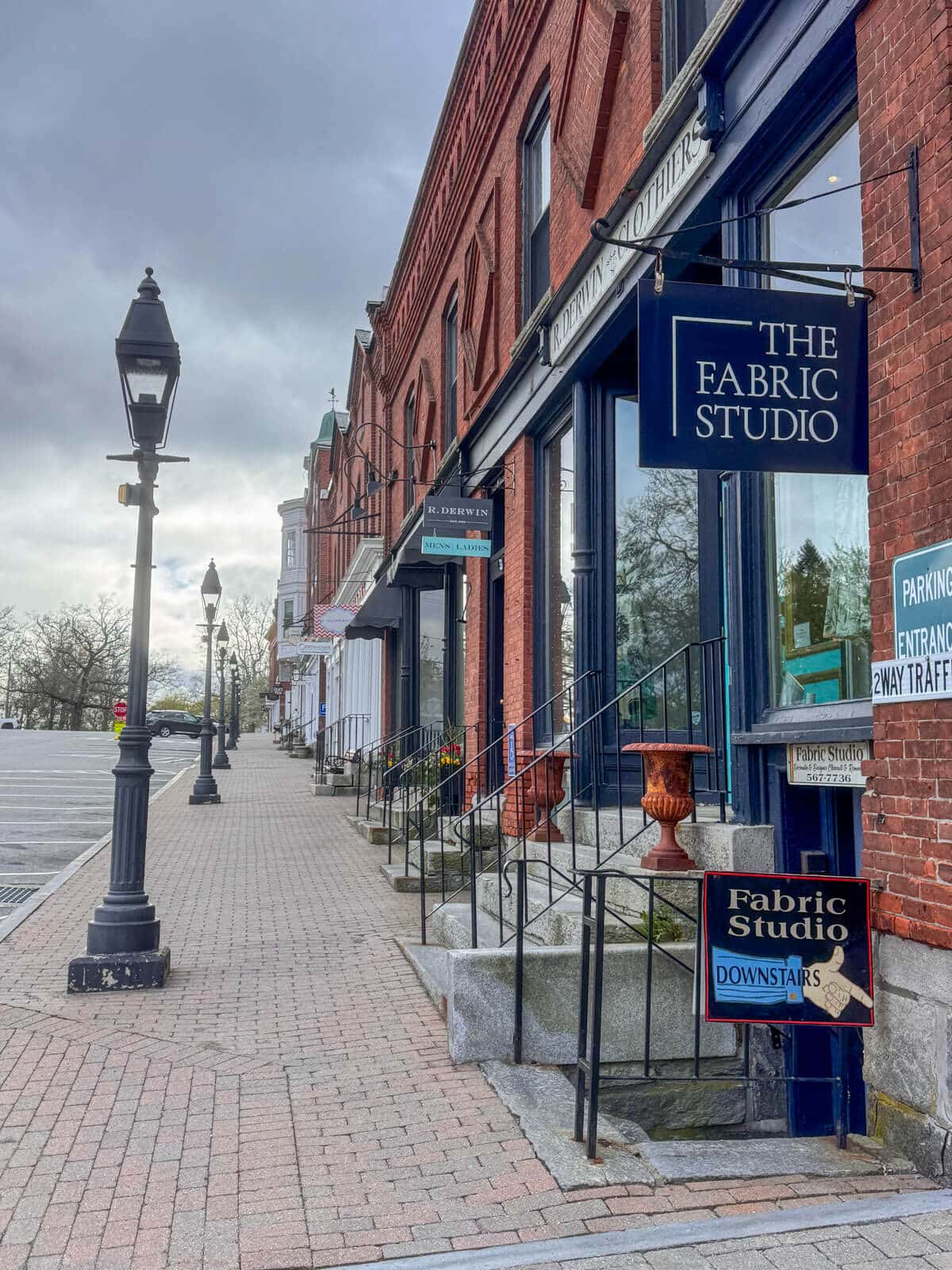cobblestone street in downtown litchfield with brick buildings and various signs and storefronts and black lampposts lining the sidewalk.