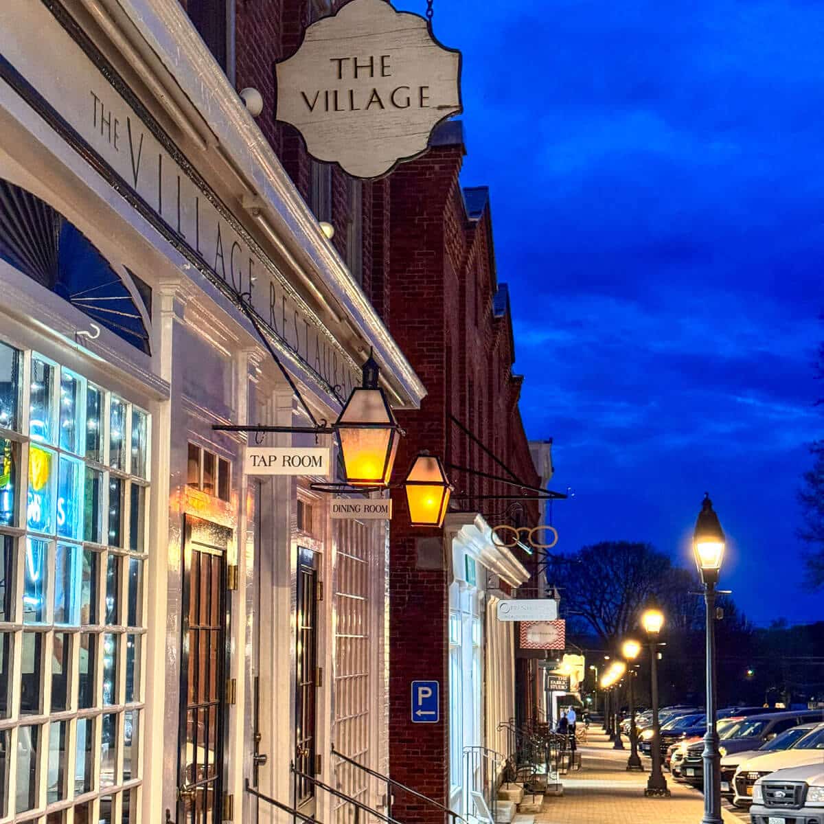 downtown litchfield connecticut at dusk with lampposts lining stone sidewalk and brick storefronts on the left.