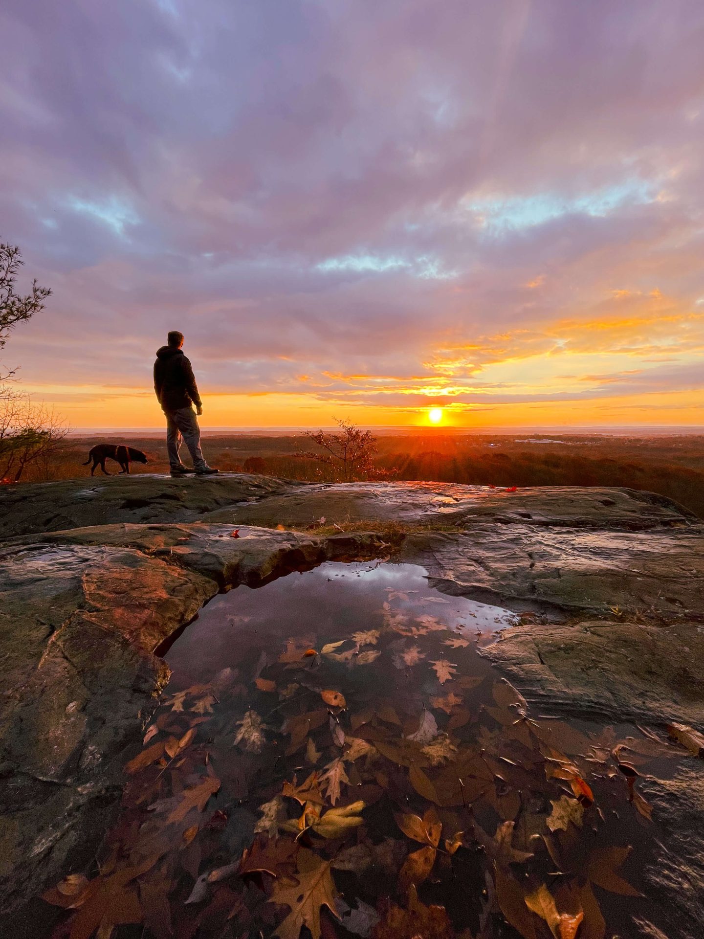 man at top of rattlesnake mountain in ct at sunrise time with orange colors in sky