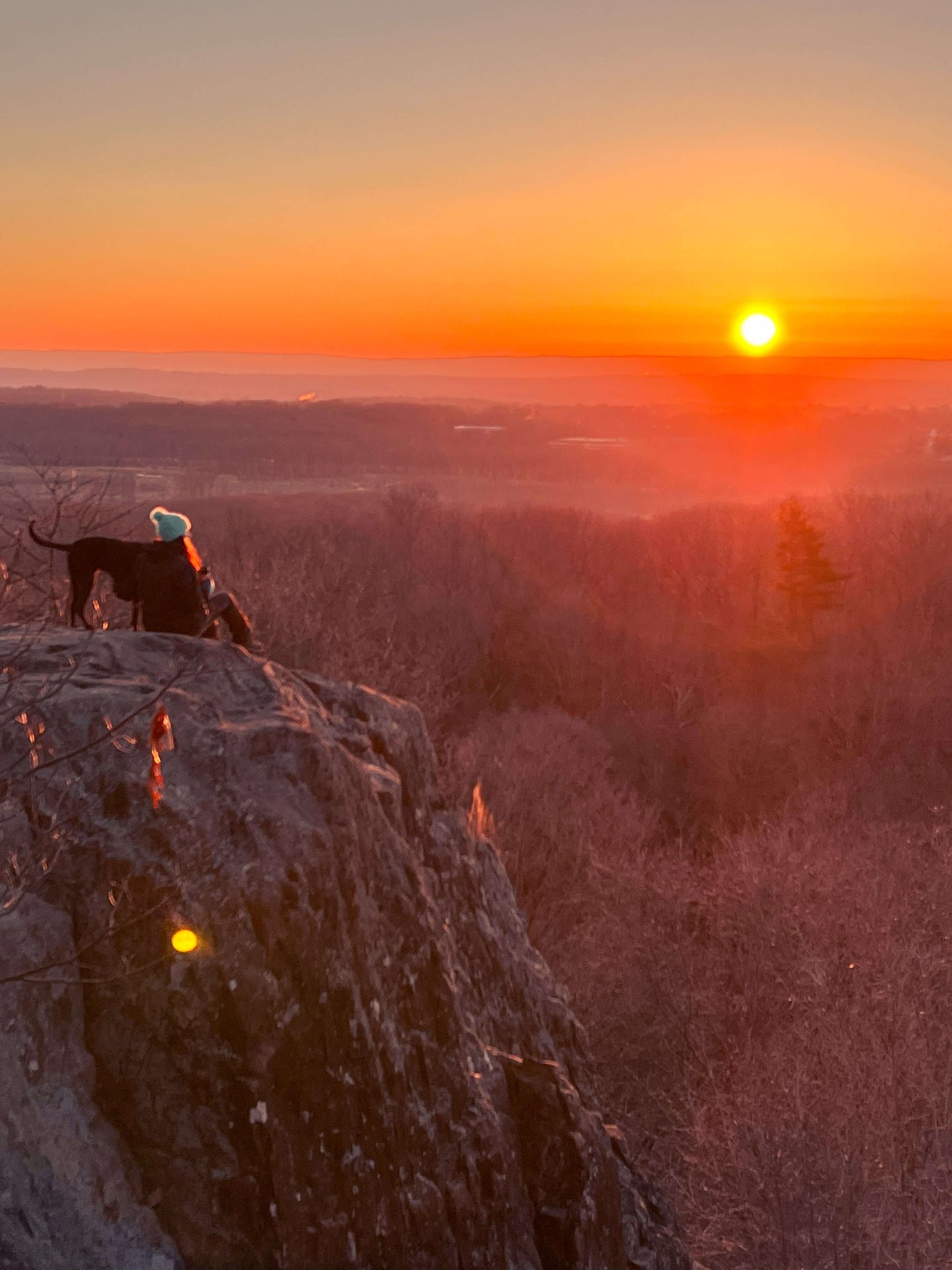 woman and dog on rattlesnake mountain at sunrise time with orange colors in sky