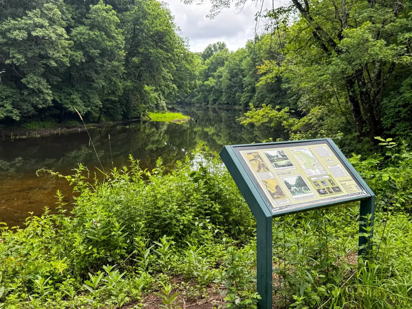 fisher meadows trail sign along the farmington river on summer day with green trees lining the river.