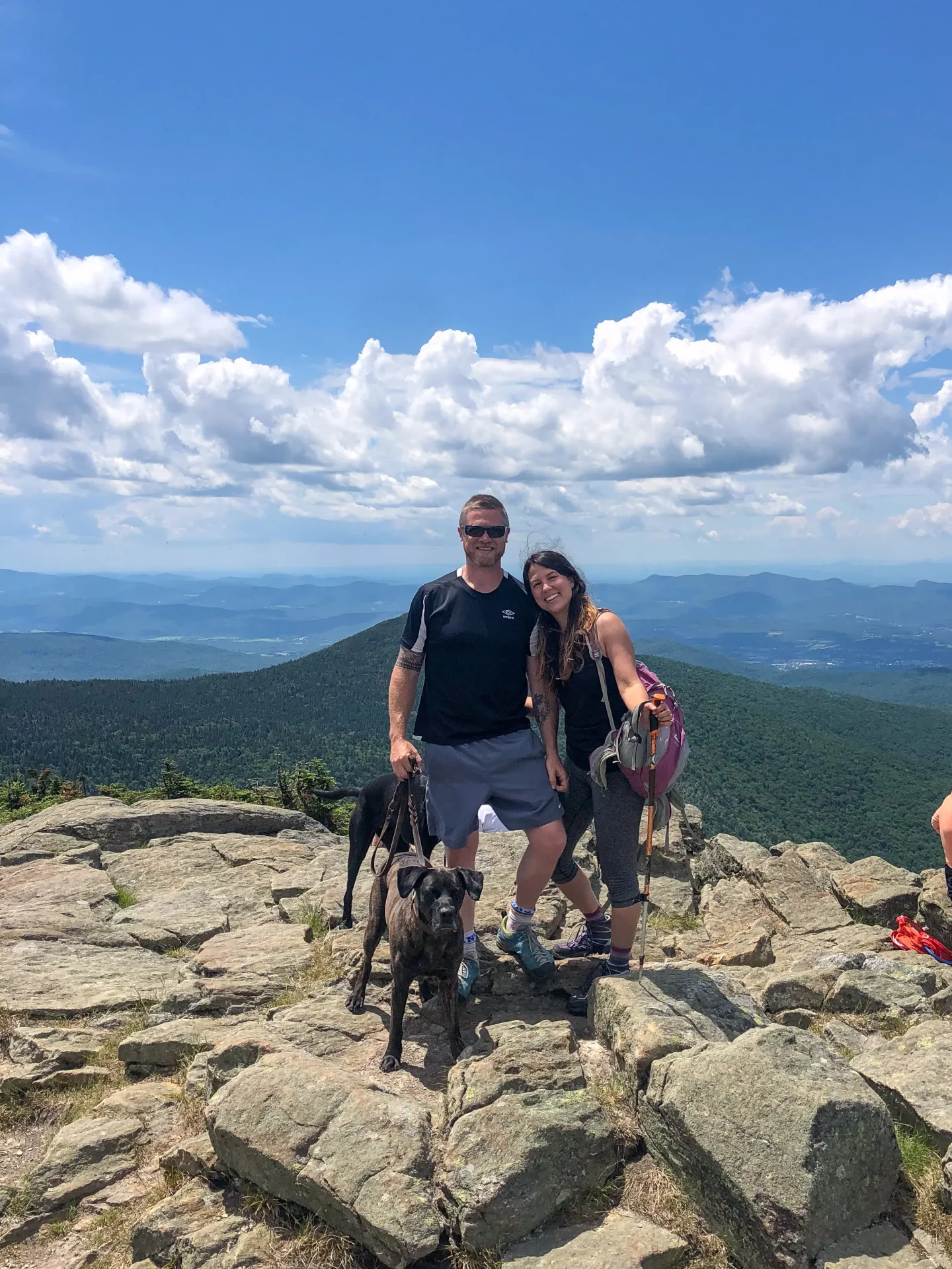 man and woman and dogs atop killington hike in vermont in summer