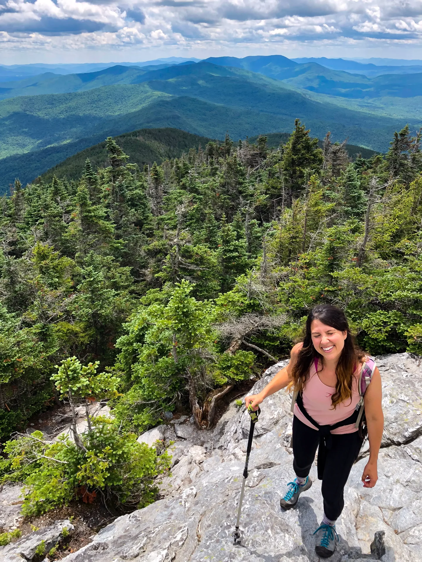 woman smiling on top of mount abraham hike in vermont with green mountains and blue sky