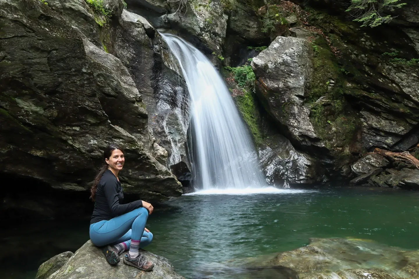 woman sitting by bingham falls in stowe vermont with green pool of water