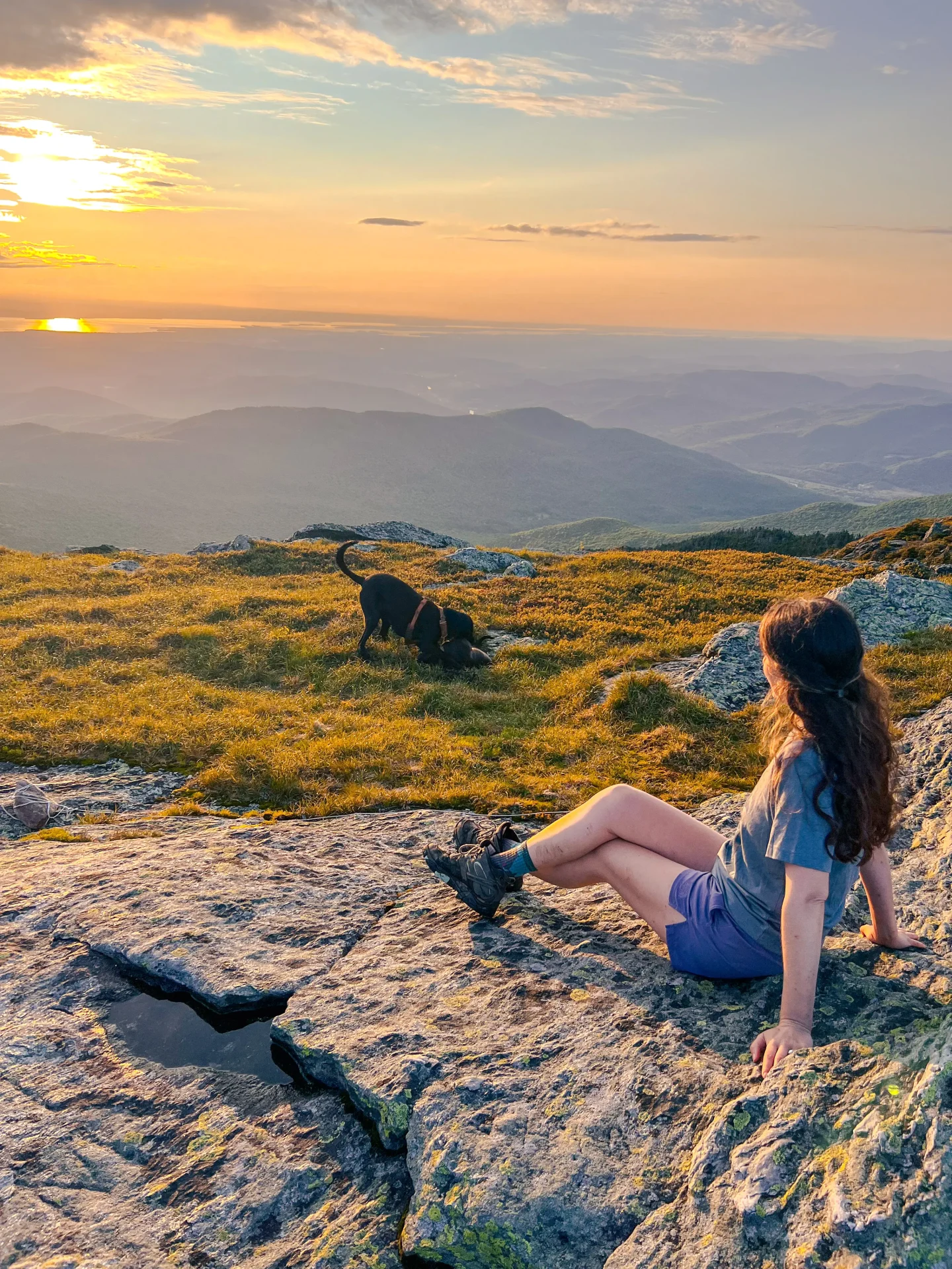 woman on top of camels hump in vermont at sunset with golden sun and green mountains