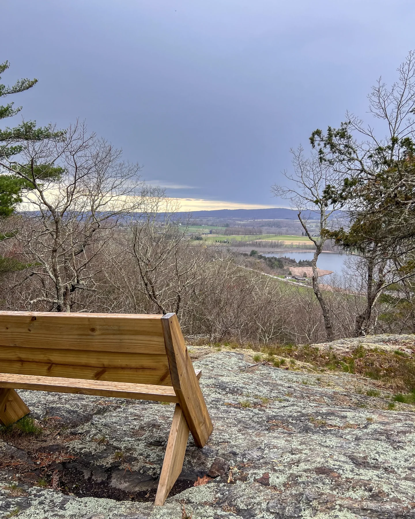 wooden bench high on a cliff overlooking water and mountains at land trust in sharon connecticut