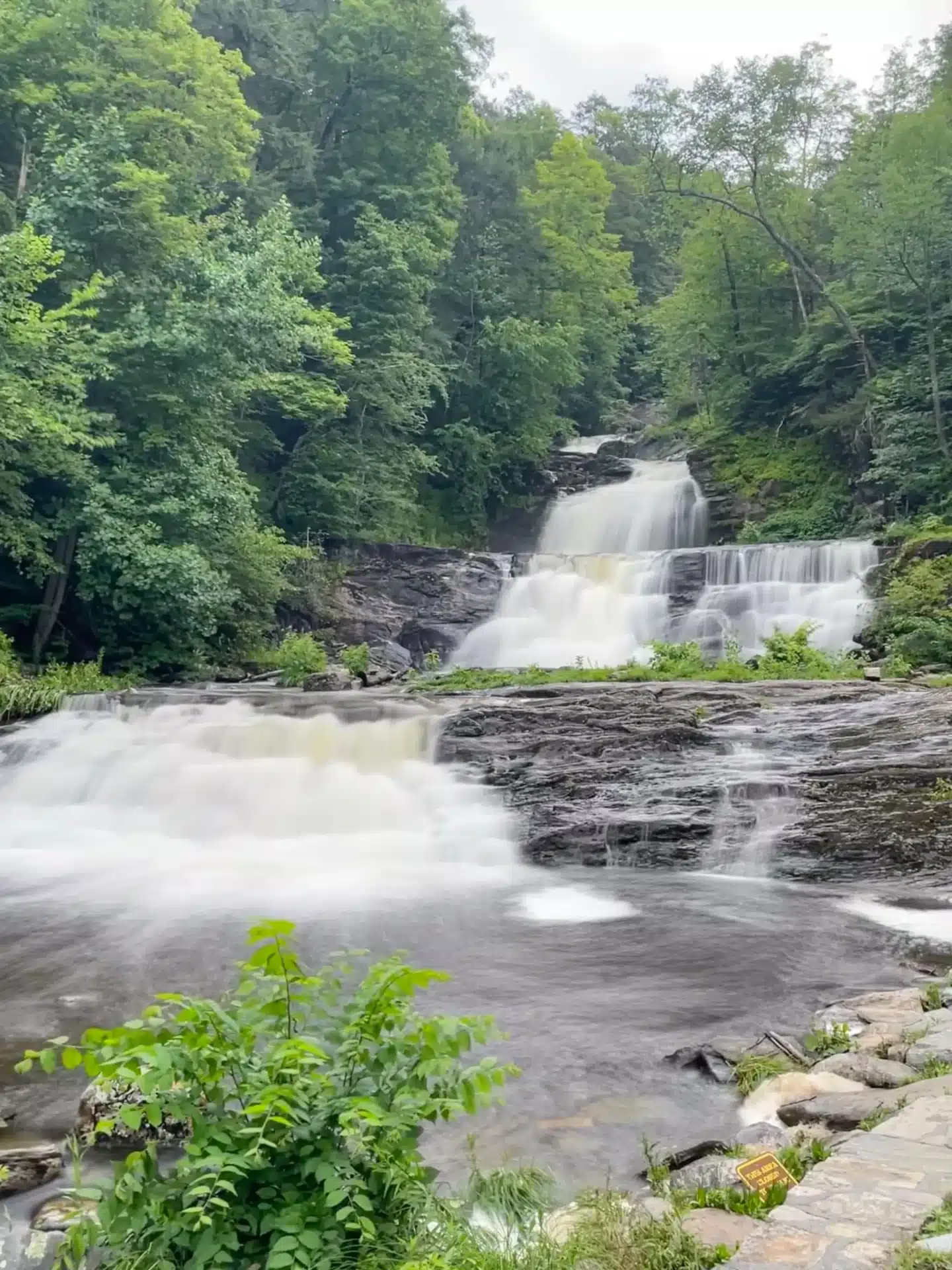 long exposure waterfall photo with smooth cascading water at kent falls in summer with green trees lining the waterfall.
