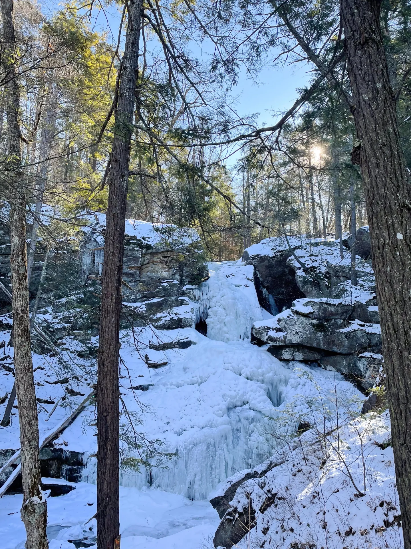 frozen kent falls waterfall in winter with tall pines trees around and blue sky above