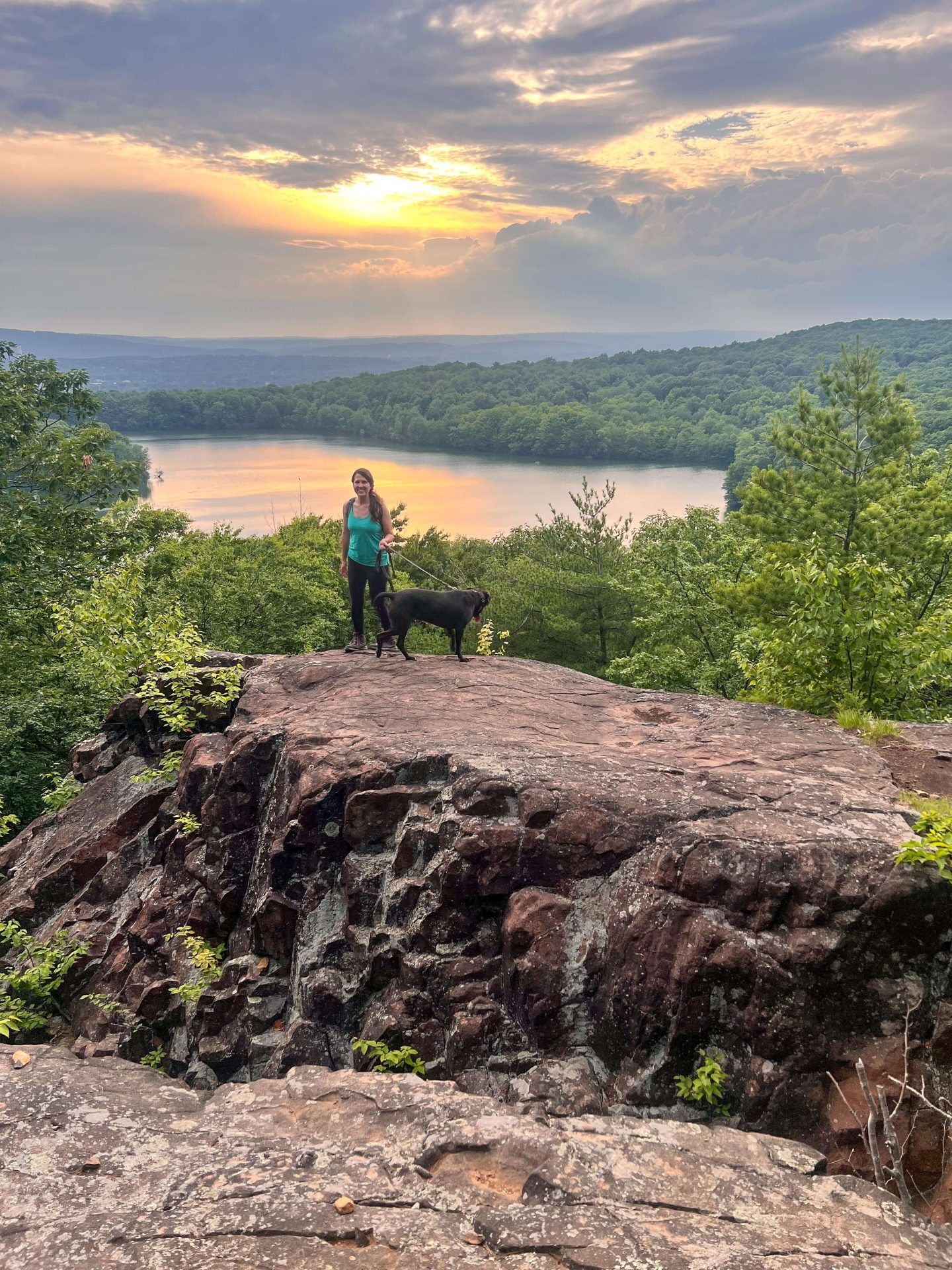 woman and dogs on mountain in connecticut for sunset with lake in distance