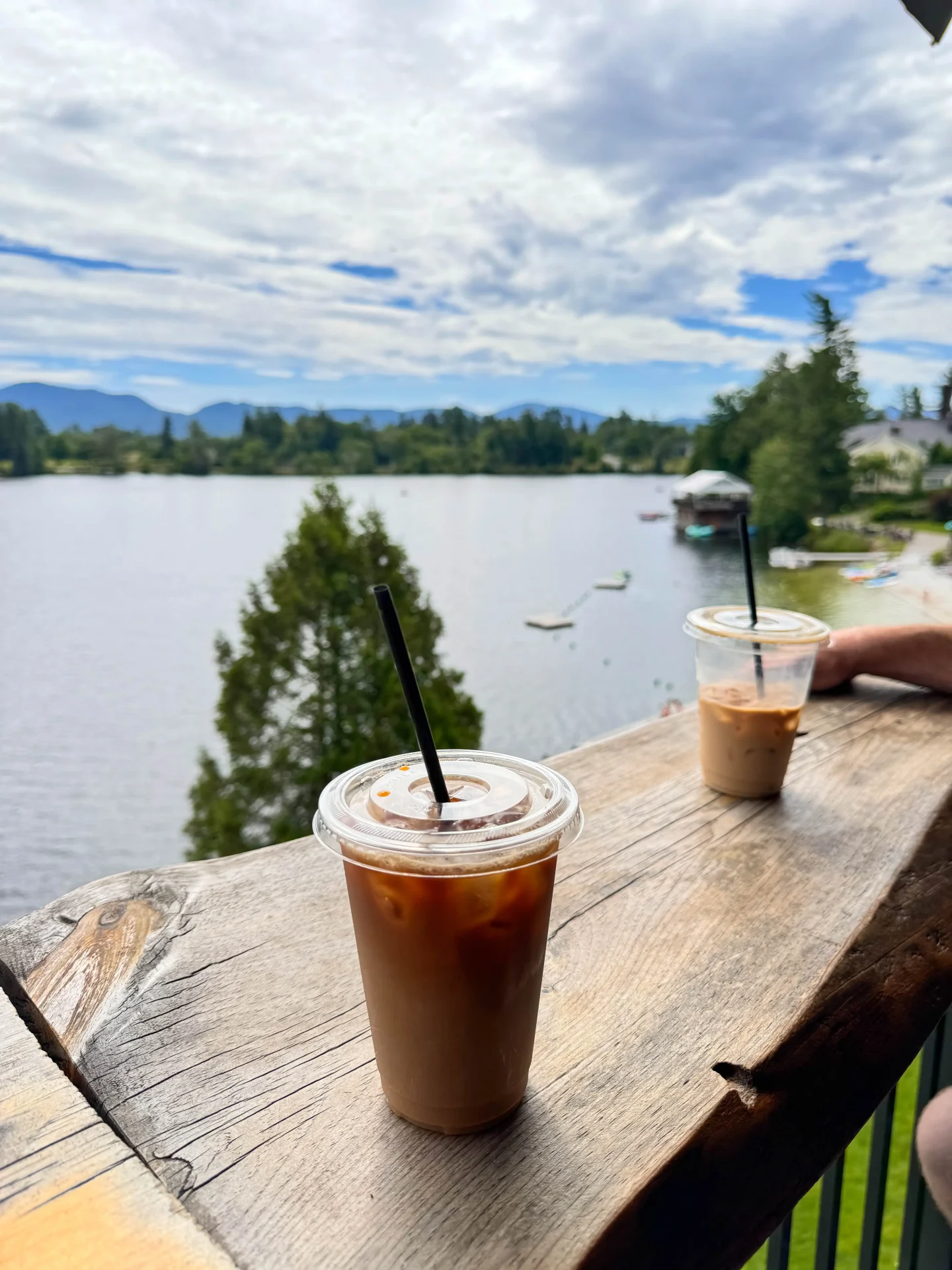 two iced coffees on the deck of the coffee bar in lake placid with a view of the lake and mountains in summer