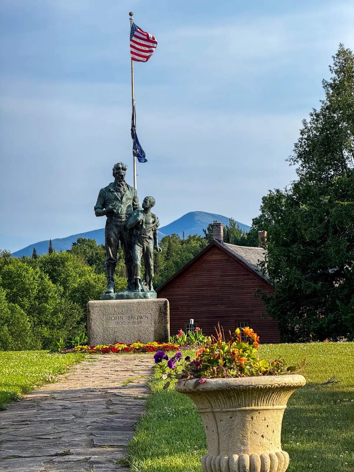 statue of man and boy with a flag pole behind them and mountain range in distance on a summer day with green grass and a light blue sky.