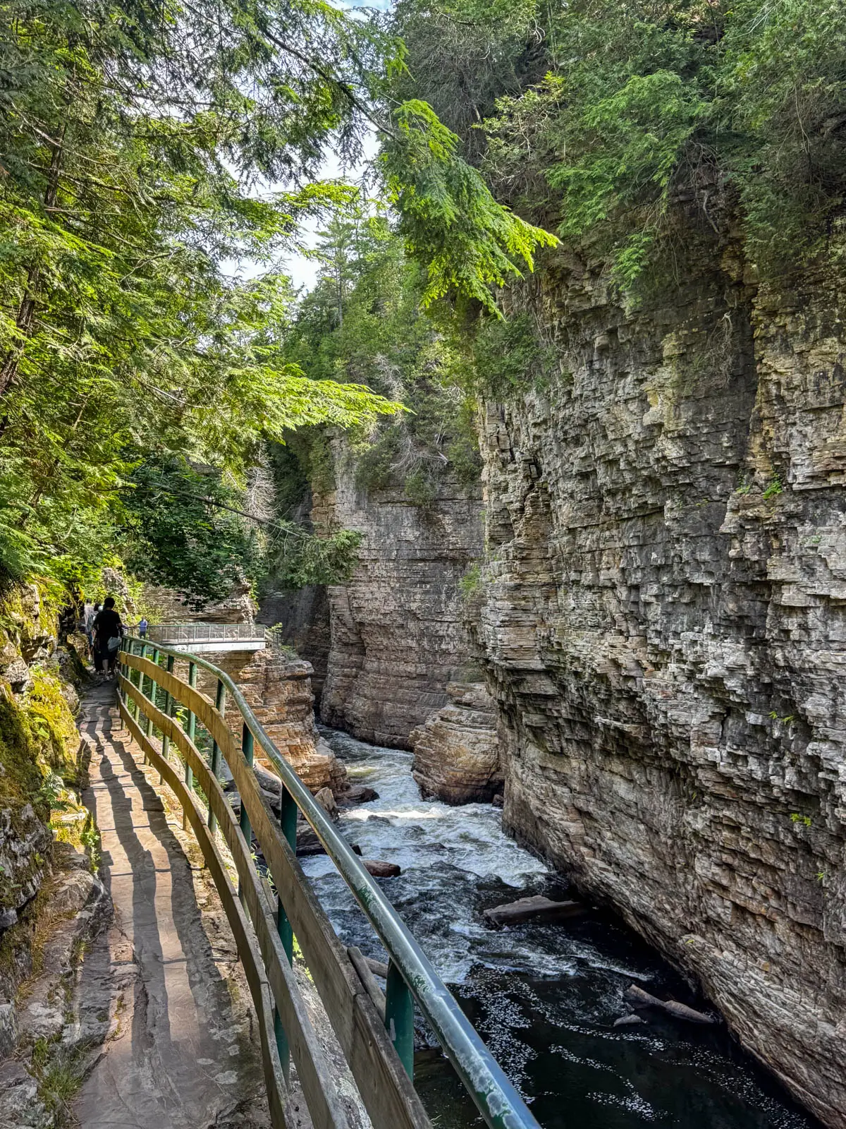 wooden cliffwalk at ausable chasm with water below and wall of rock on right.