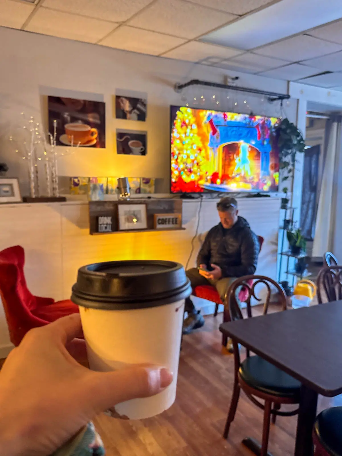 woman's hand holding a white to-go cup with black lid inside cafe.