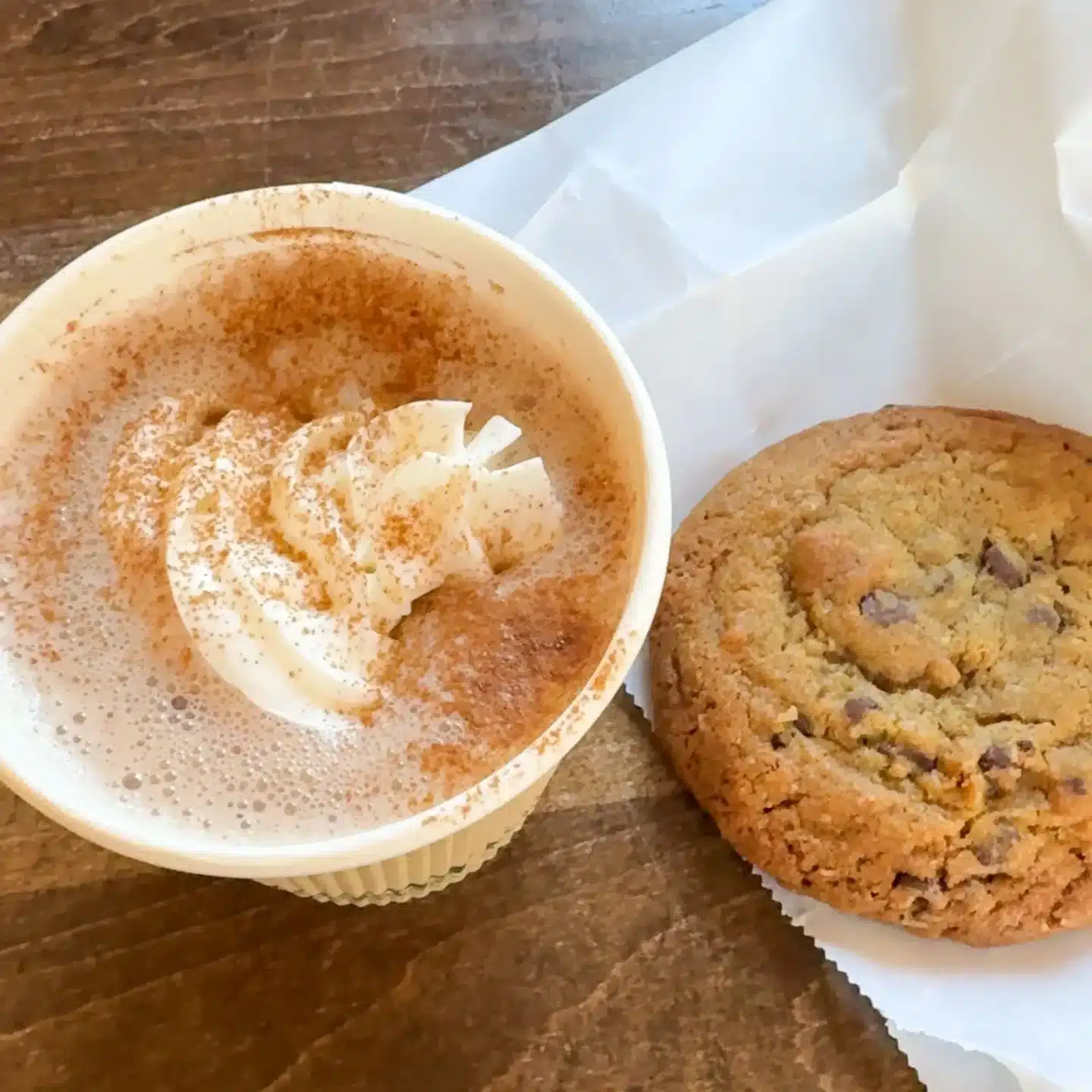 hot chocolate with whipped cream and a chocolate chip cookie on the table