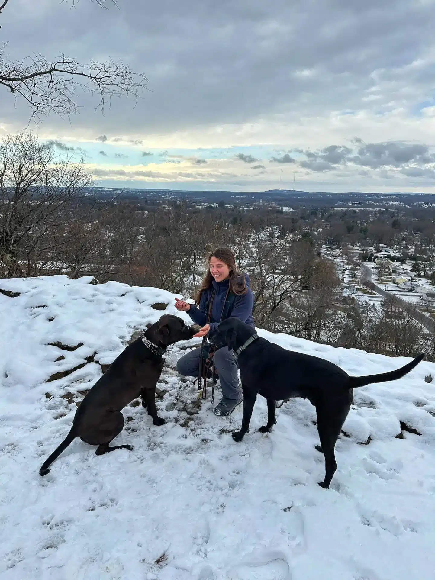 woman on mountain in newington connecticut smiling with her two black dogs