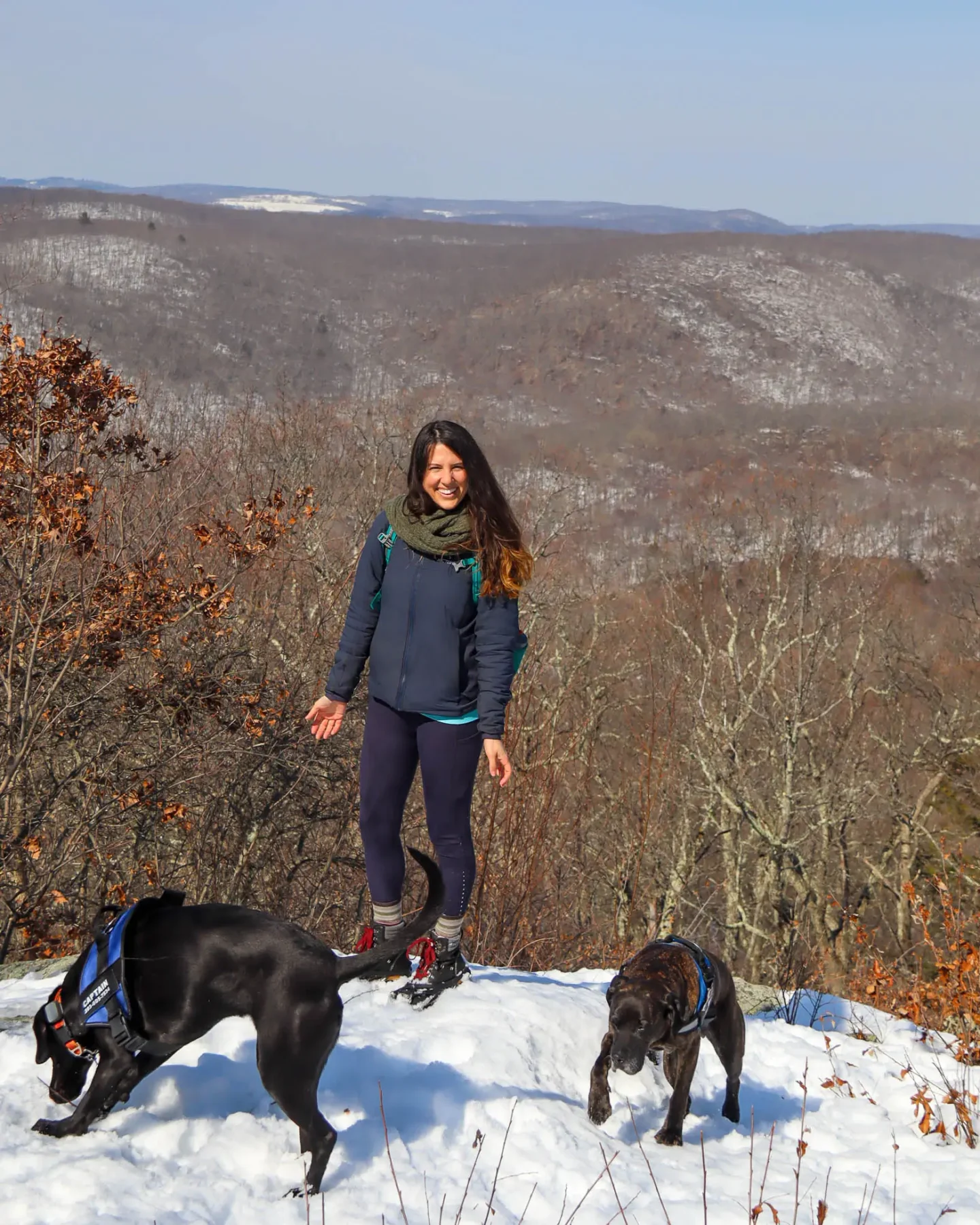 woman smiling with two dogs on winter hike at pond mountain in ct