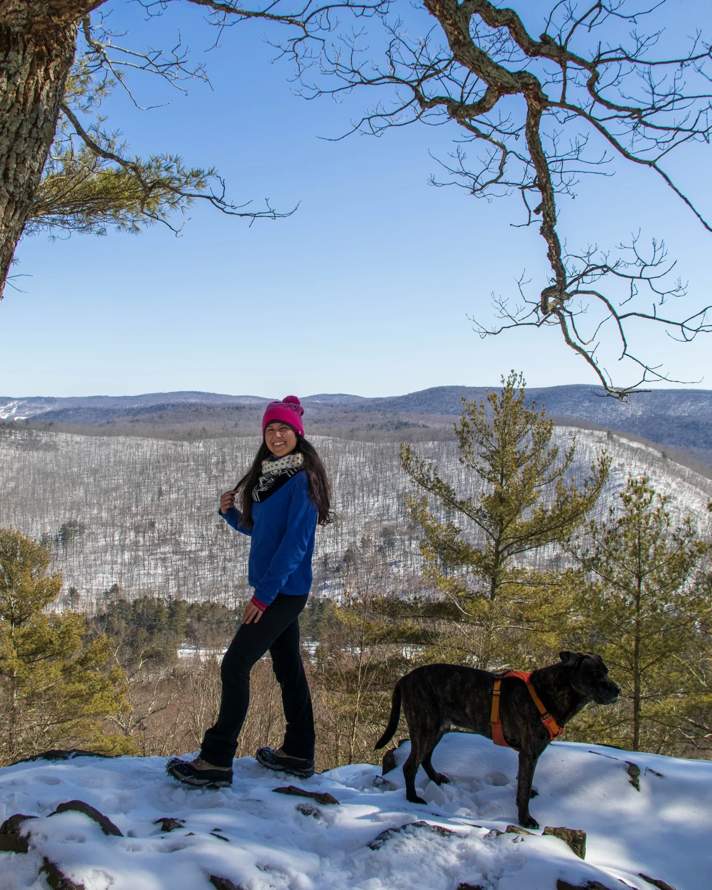 woman smiling in blue fleece and pink snow hat with snowy mountains in the distance at pine knob loop in cornwall connecticut