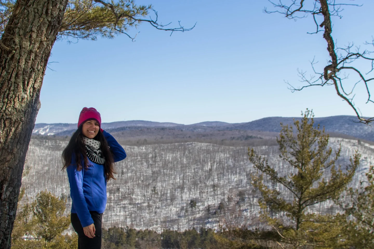 woman smiling in blue fleece and pink snow hat with snowy mountains in the distance at pine knob loop in cornwall connecticut