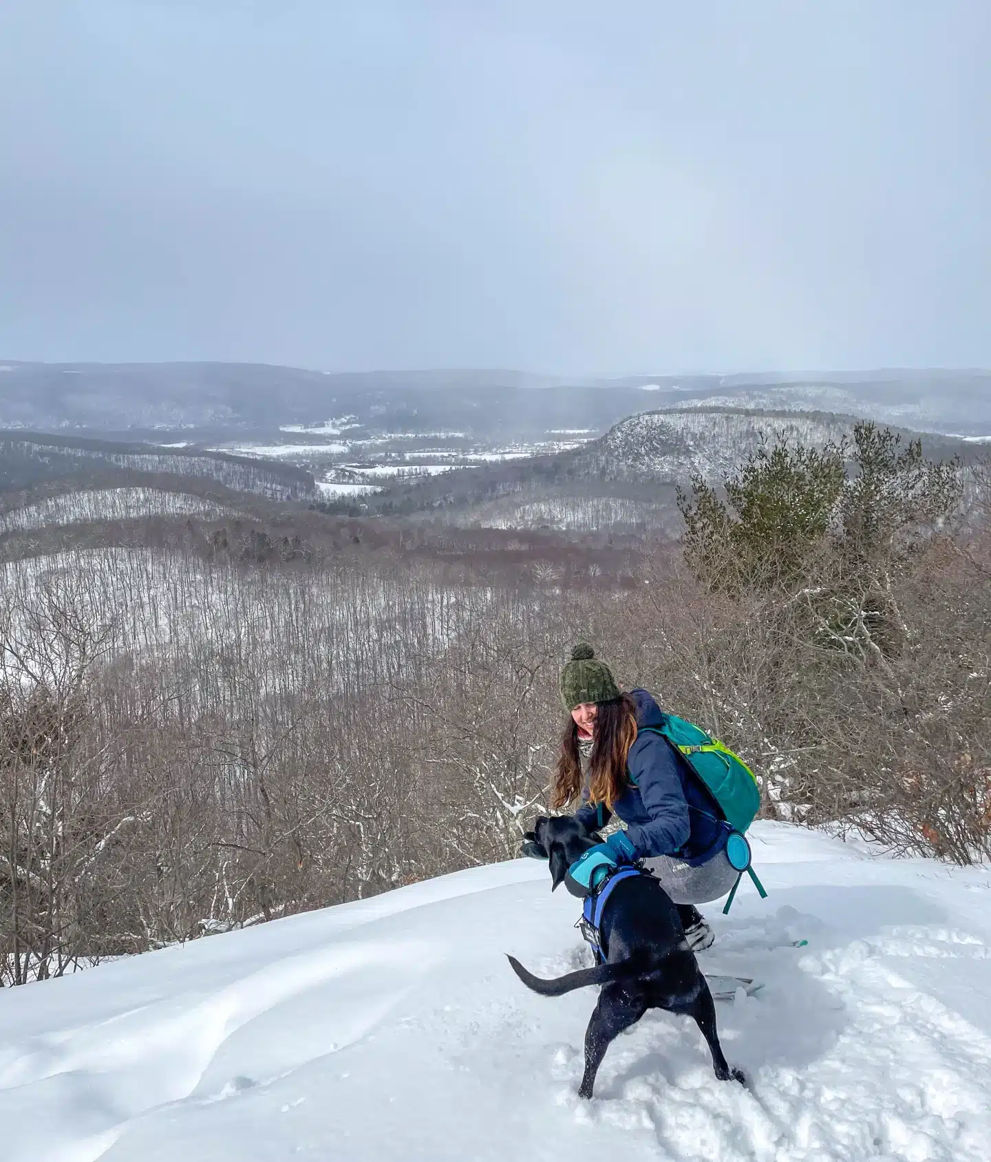 woman in winter hiking gear with two black dogs on snowy winter hike in kent connecticut