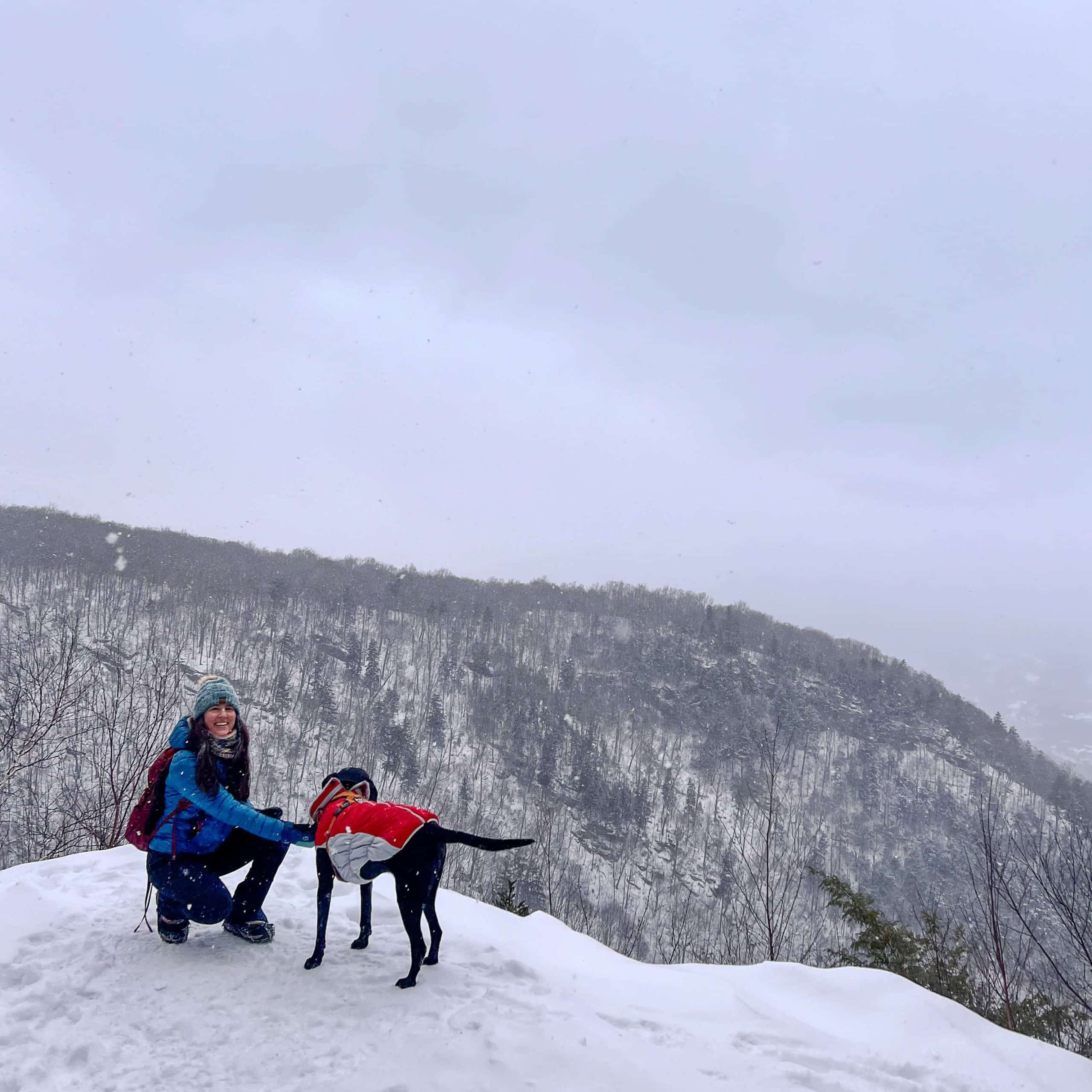 woman and black dog on snowy hike at prospect mountain in manchester vermont