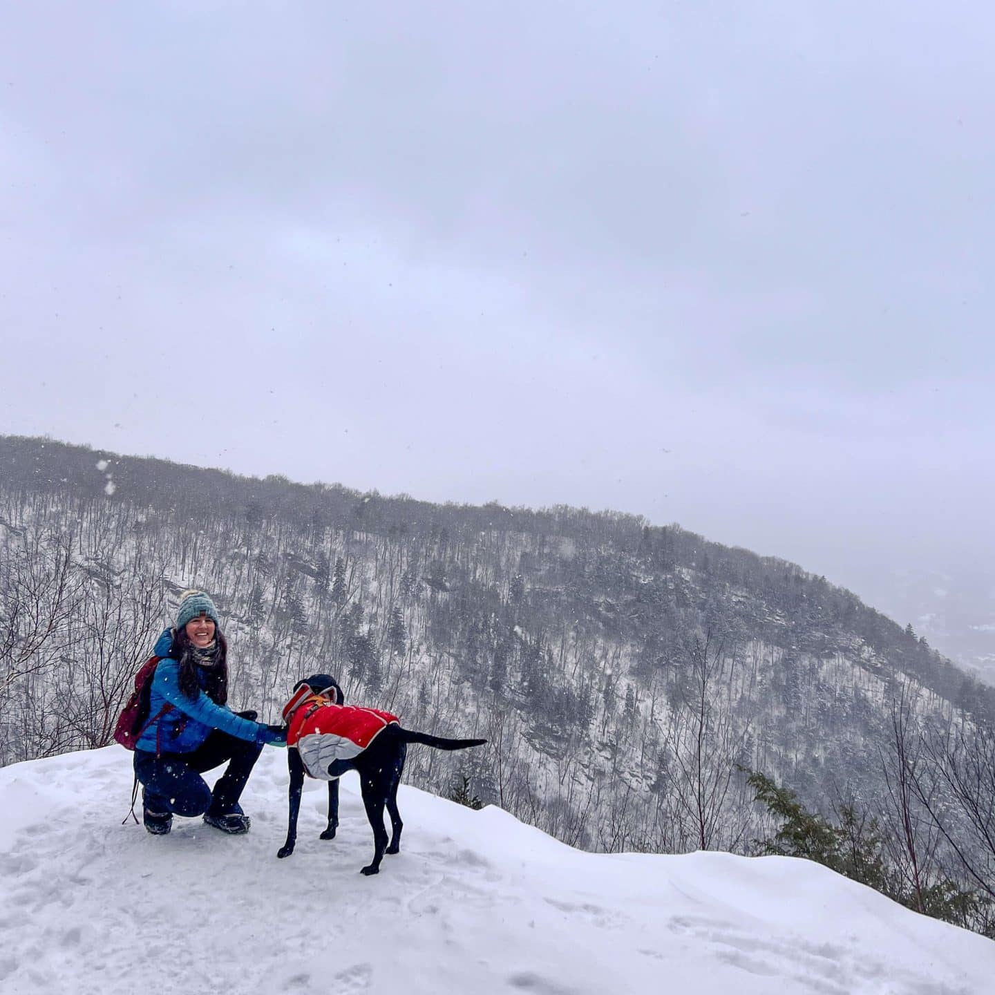 woman and black dog on snowy hike at prospect mountain in manchester vermont