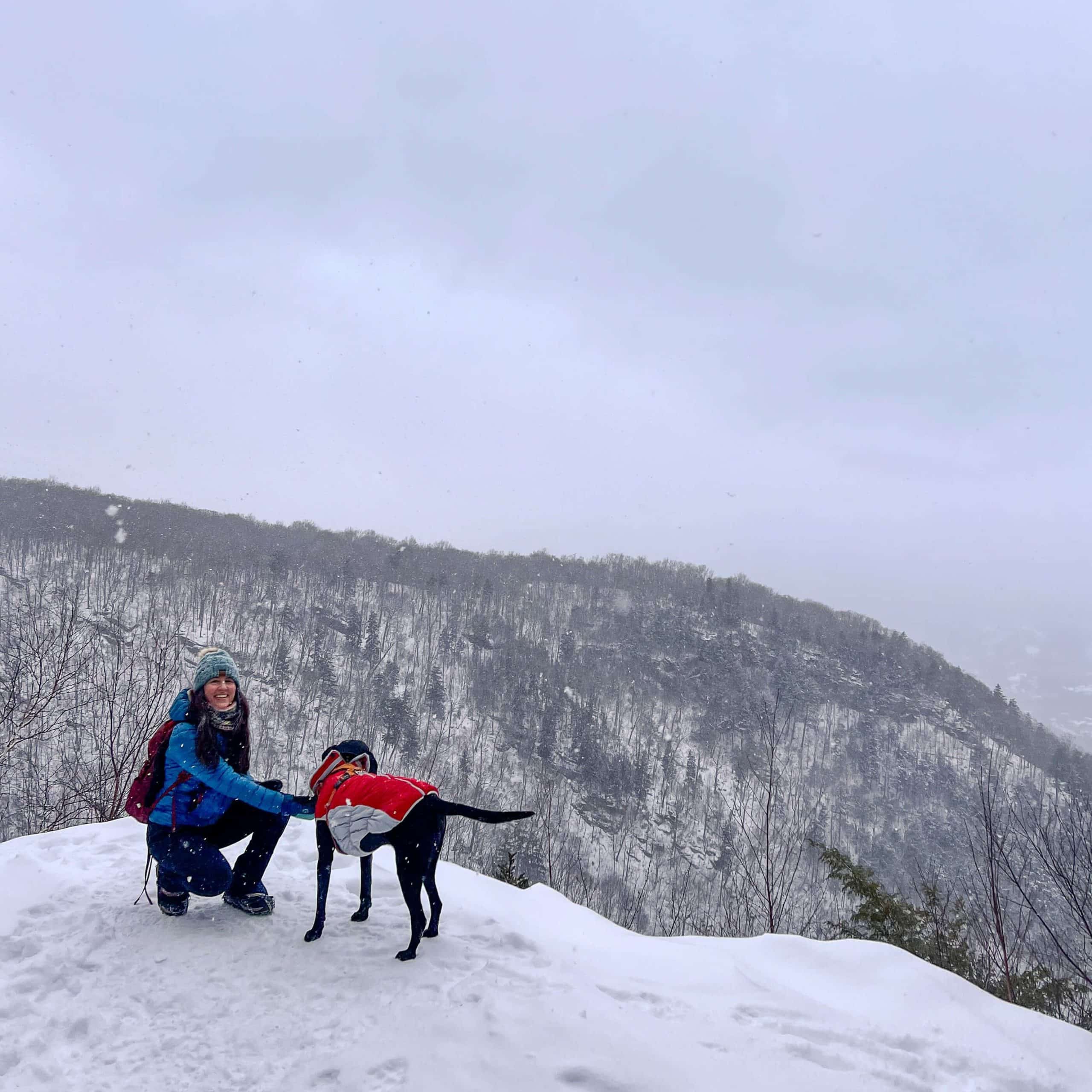 woman and black dog on snowy hike at prospect mountain in manchester vermont