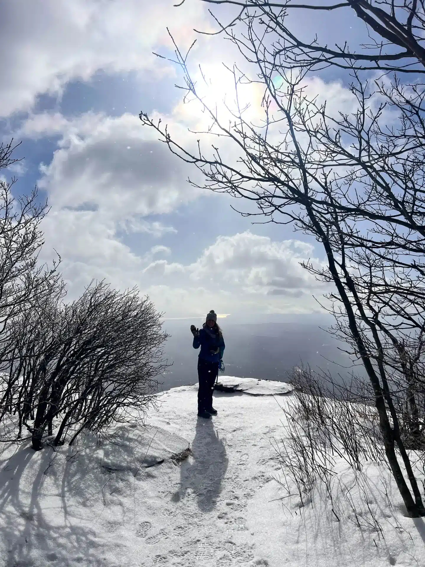 silhouette of woman in snow jacket and snow hat waving in front of view atop overlook mountain in new york