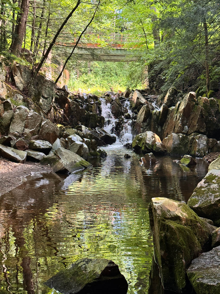 small cascades waterfall at the start of cheshire cobbles hike in massachusetts in summer surrounded by green trees