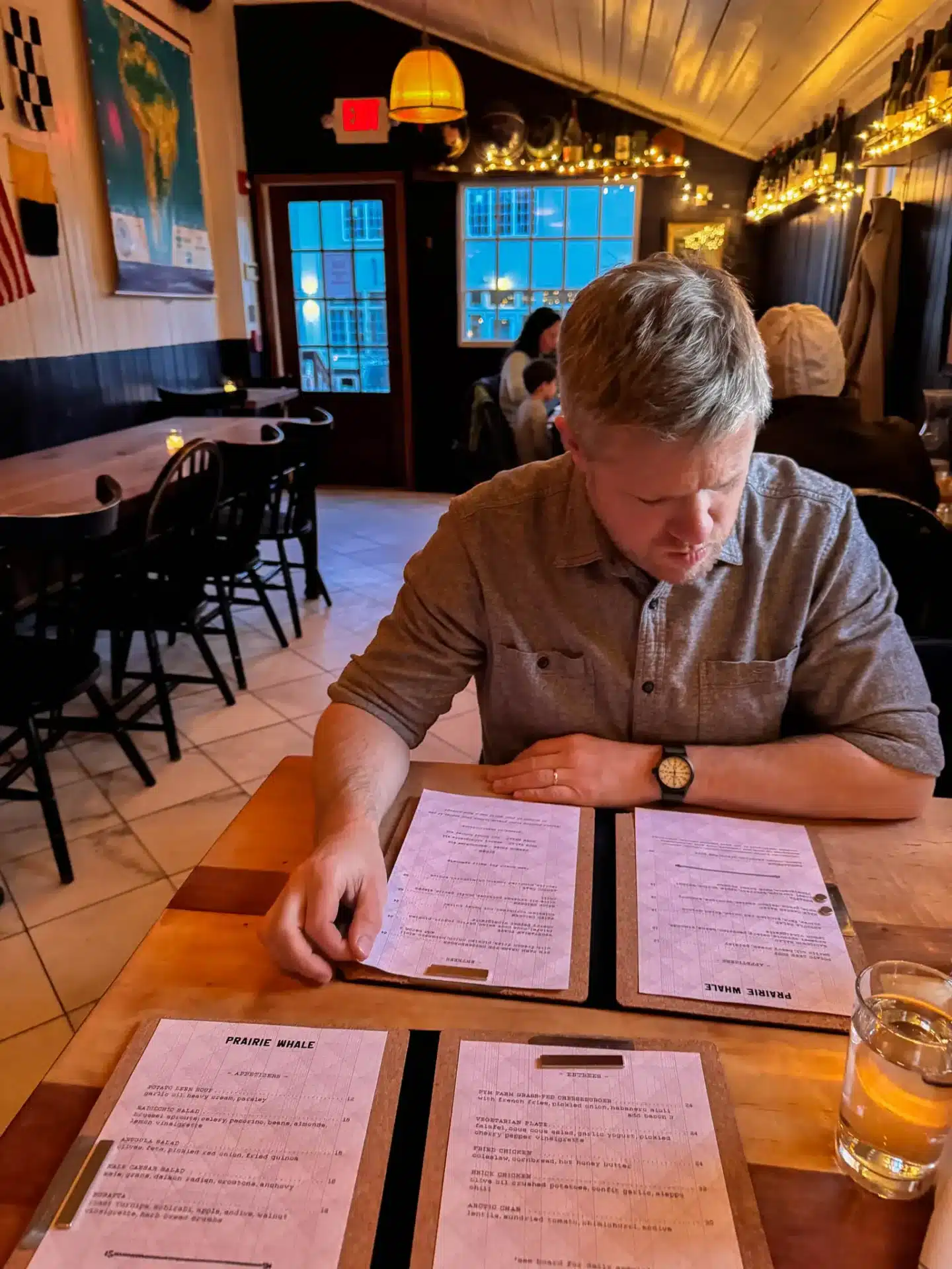 blonde man looking at the menu at the prairie whale restaurant in great barrington for dinner with ambient lighting at dinnertime