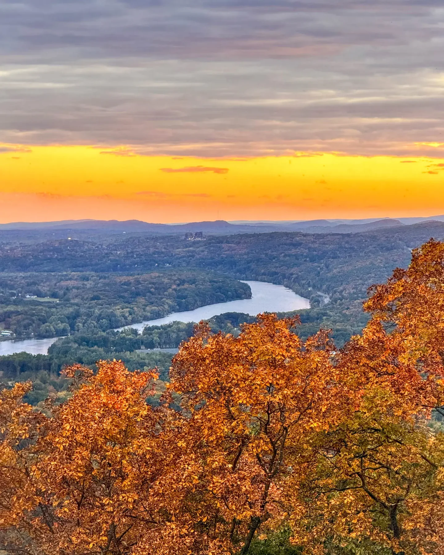 view of connecticut river from mount holyoke at sunset time in fall with orange leaves and golden sunset sky