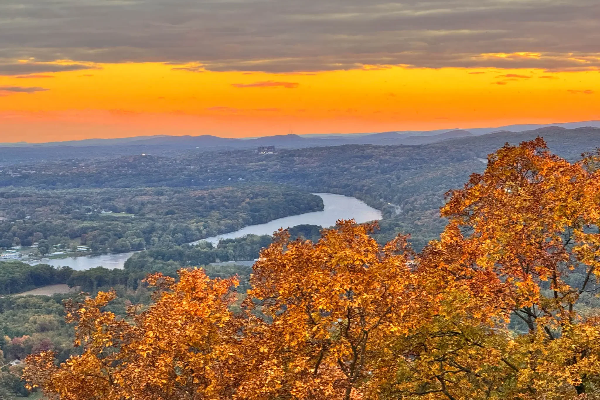 view of connecticut river from mount holyoke at sunset time in fall with orange leaves and golden sunset sky