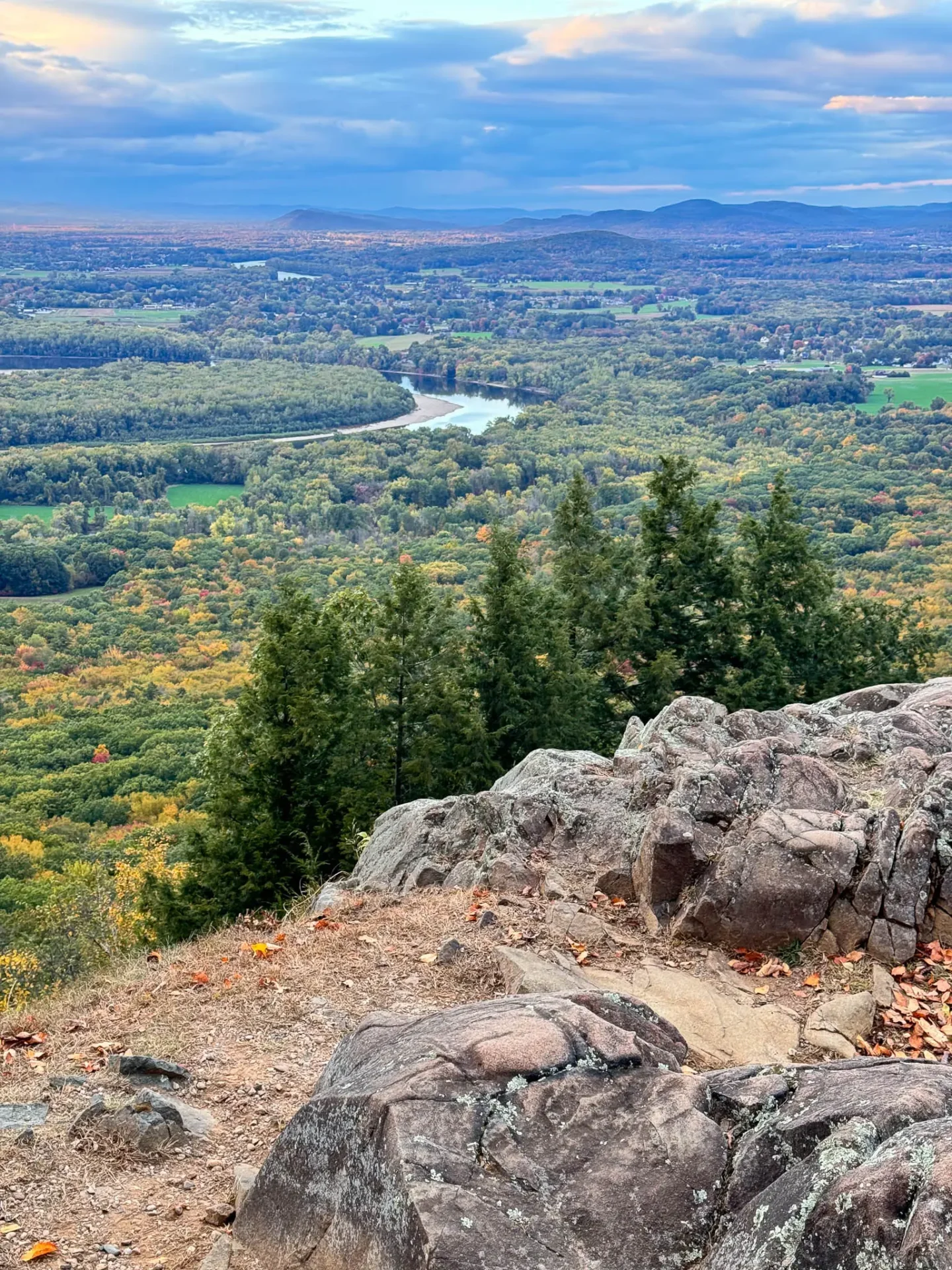 views from top of mount holyoke in early fall with green mountains and light yellow leaves in the distance